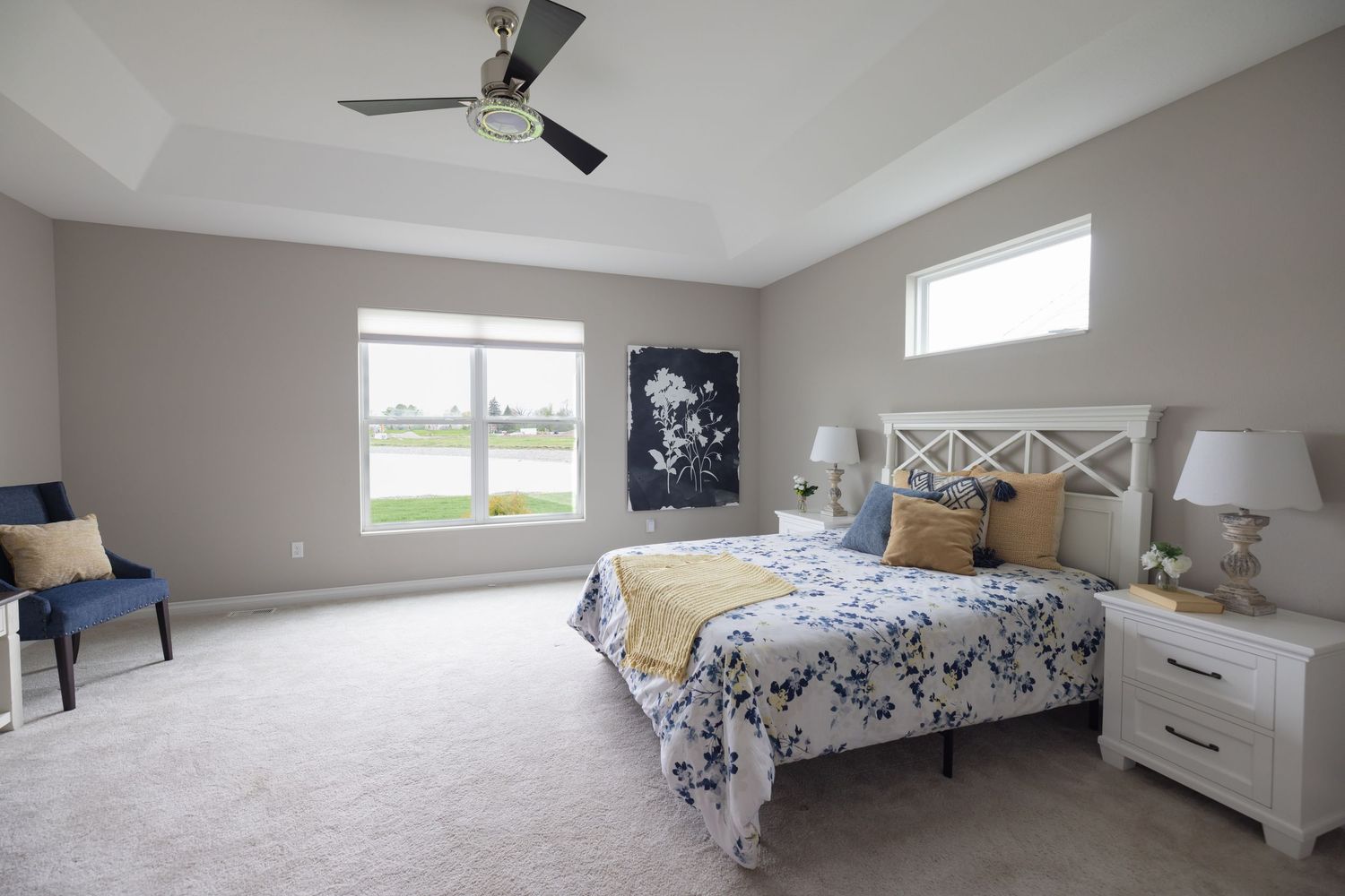 Spacious master bedroom with vaulted ceiling, ceiling fan, plush carpet, white queen bed, and large windows providing natural light.