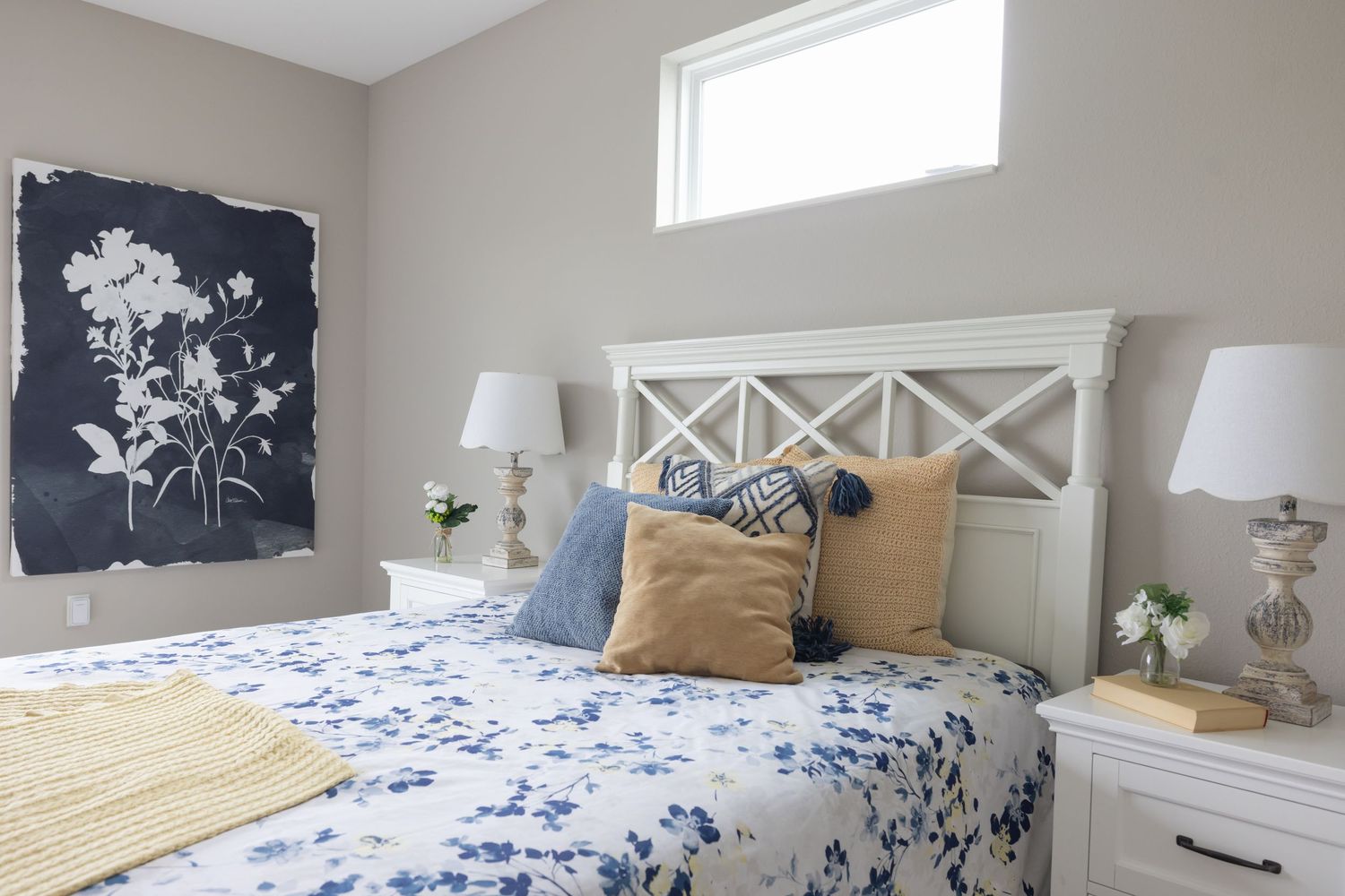 Cozy bedroom with white headboard, blue floral bedding, decorative pillows, matching nightstands, and botanical wall art.