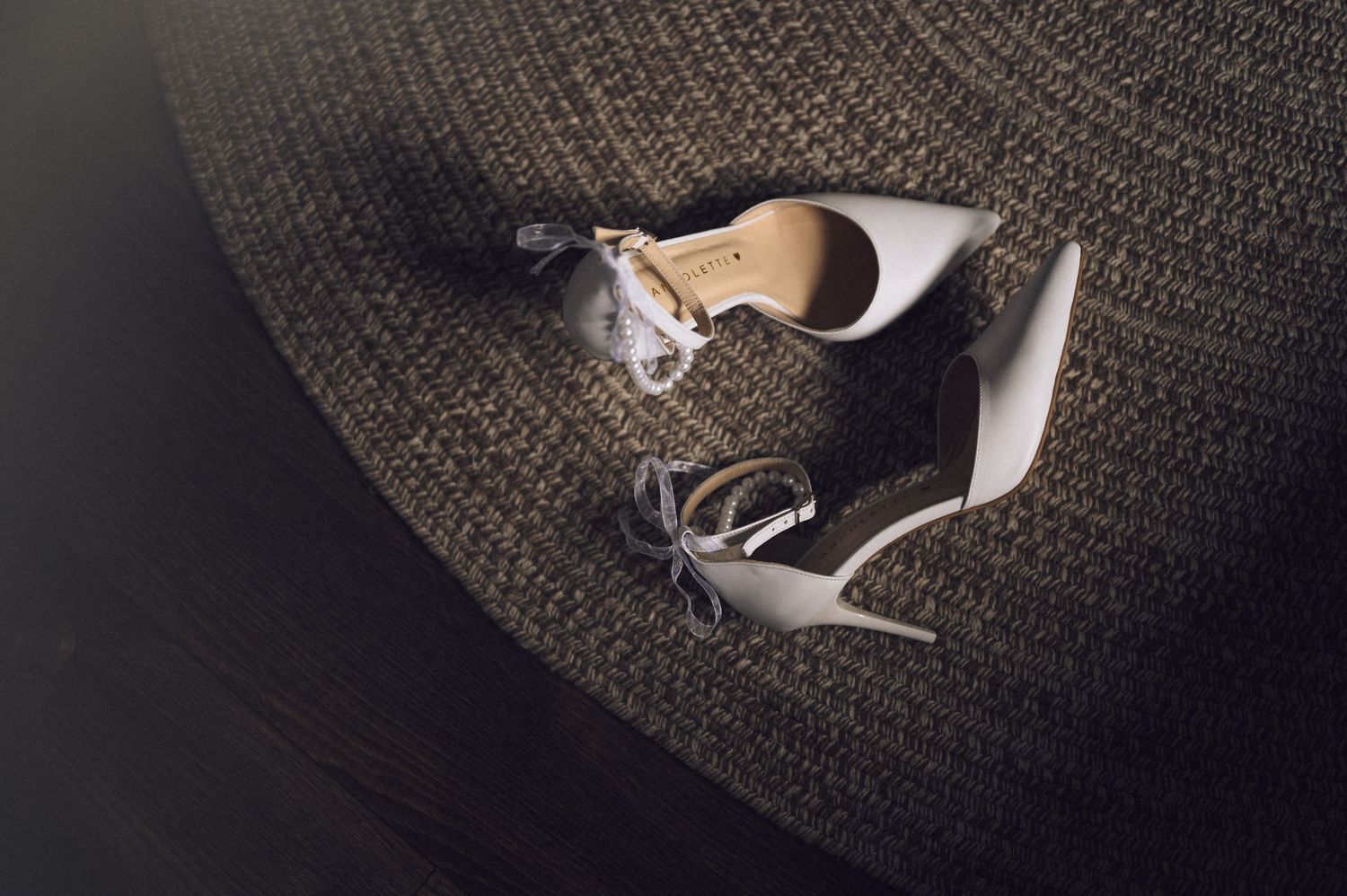 Elegant white high heel shoes with ankle straps resting on a textured gray carpet surface.