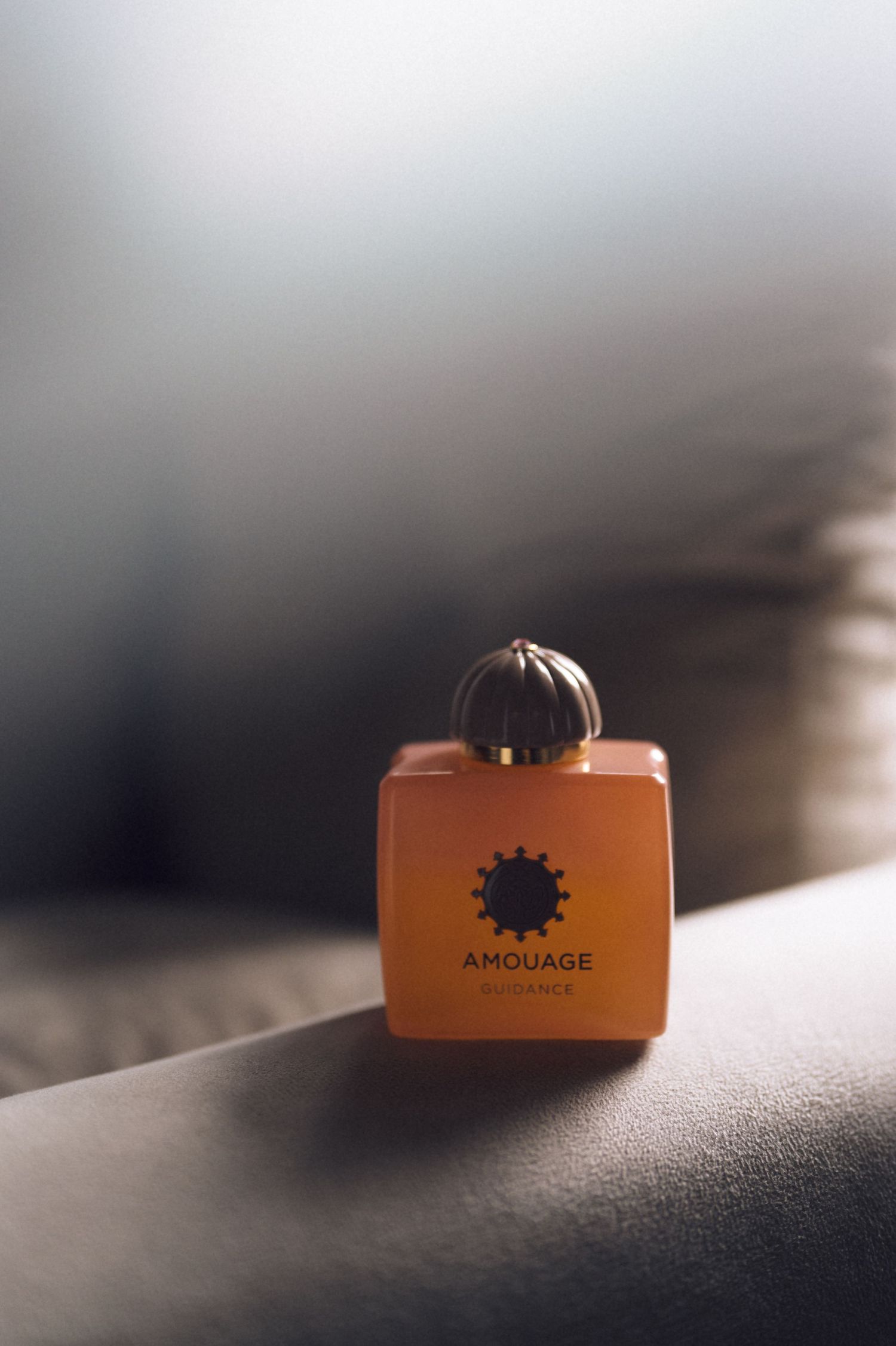 Amouage luxury perfume bottle in orange glass with ornate gold cap on a soft gray surface.