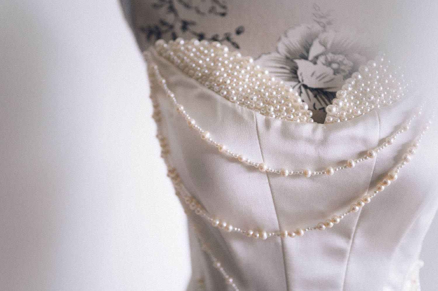 Elegant white satin wedding dress bodice adorned with pearl beading and floral embroidery on a mannequin.