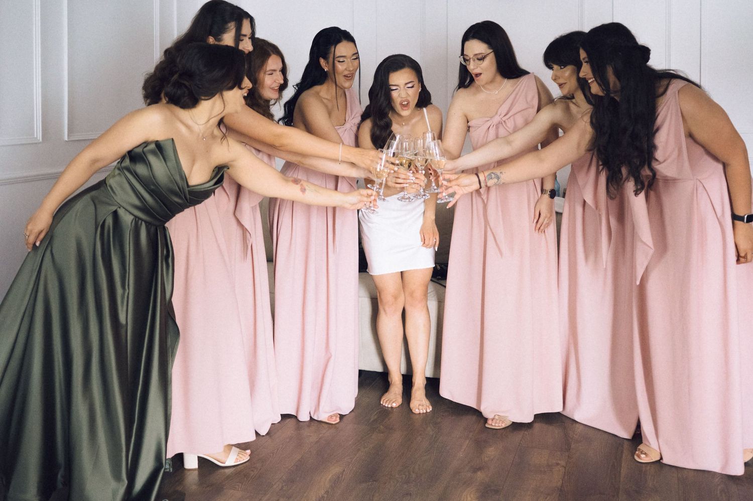 Bride in white dress toasting champagne with bridesmaids in pink and green gowns at a wedding celebration.