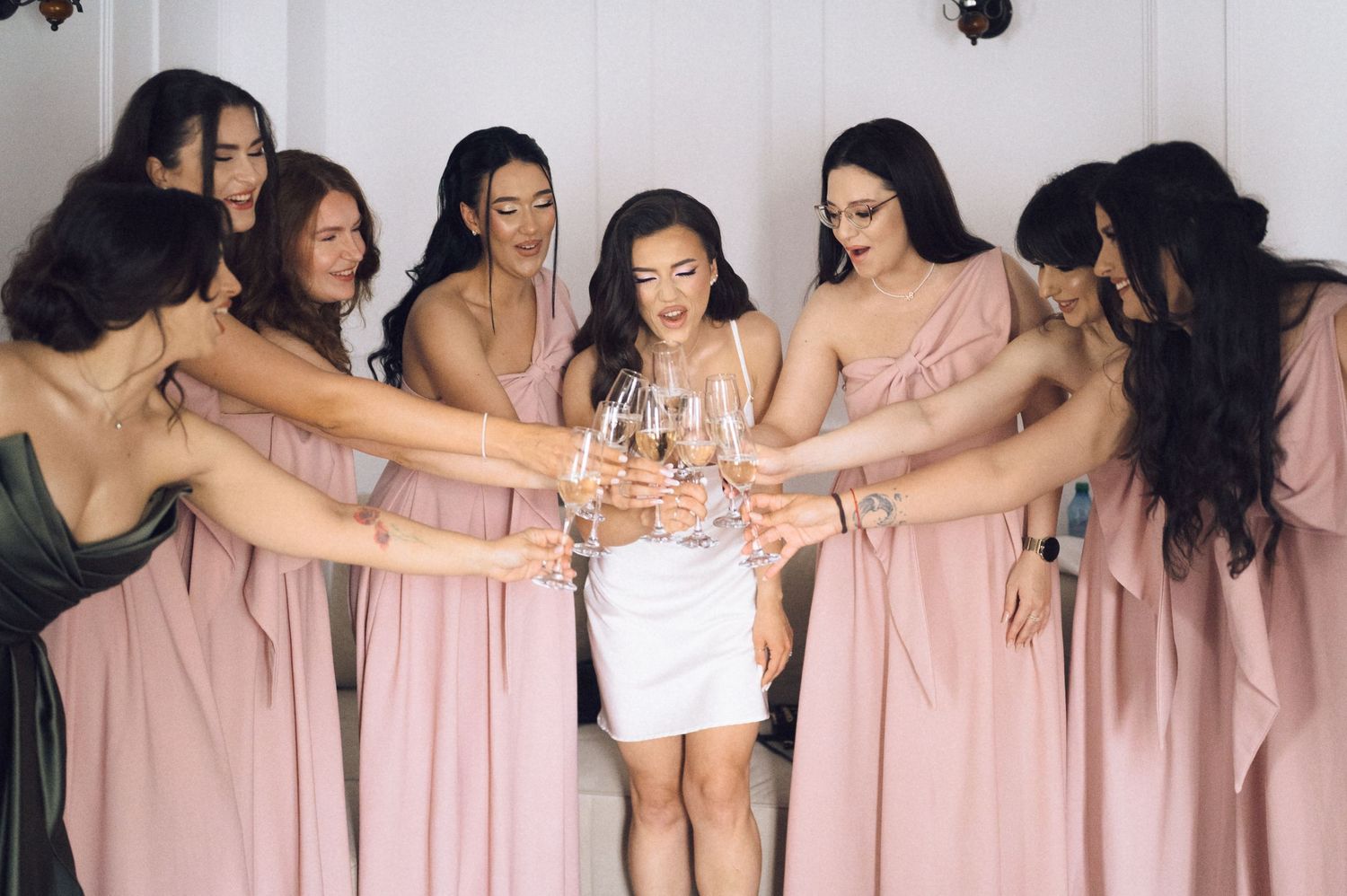 Bride in white dress toasting champagne with bridesmaids in pink gowns during a wedding celebration.
