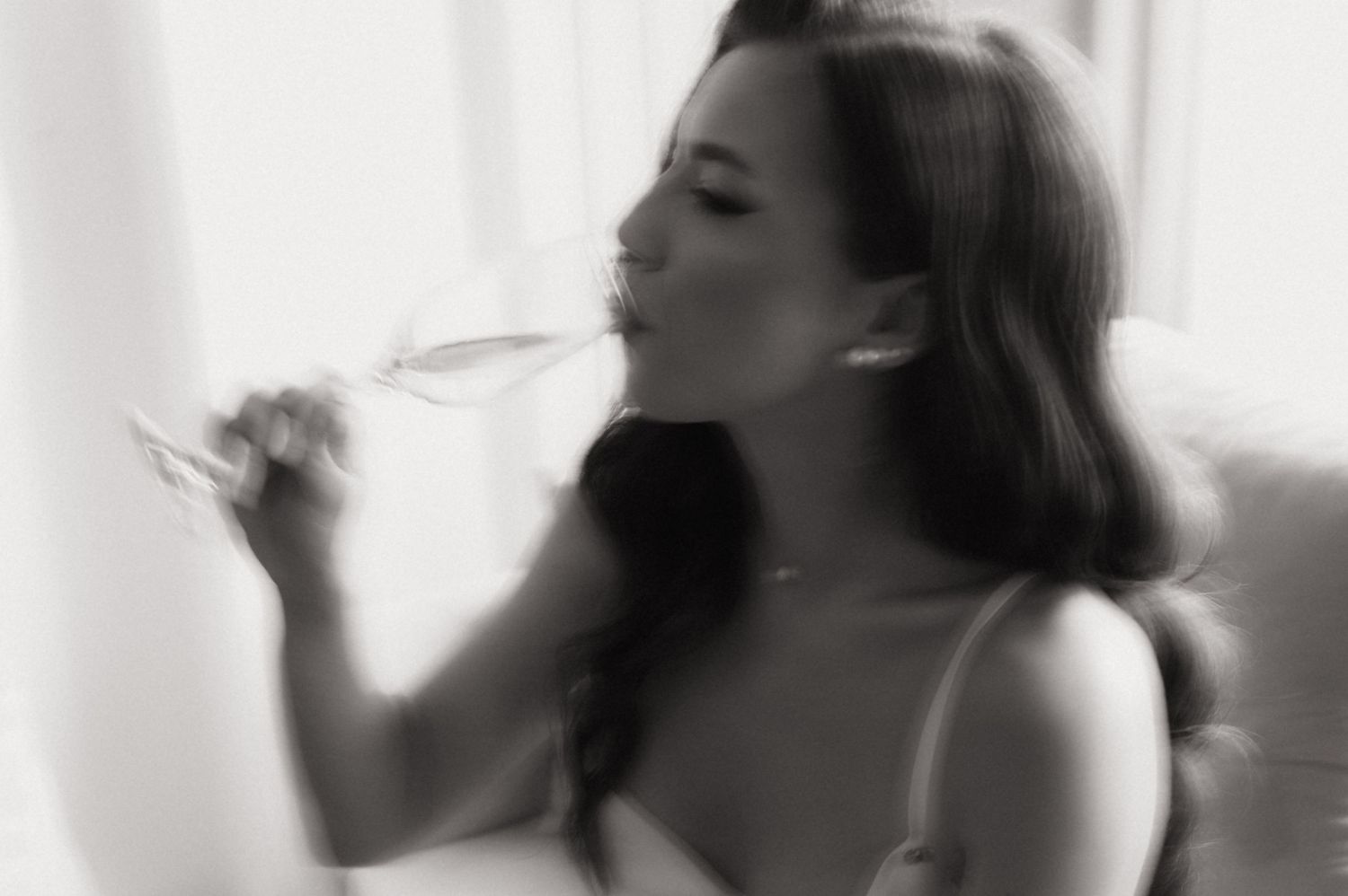 Elegant black and white photo of a woman sipping white wine in soft natural light.