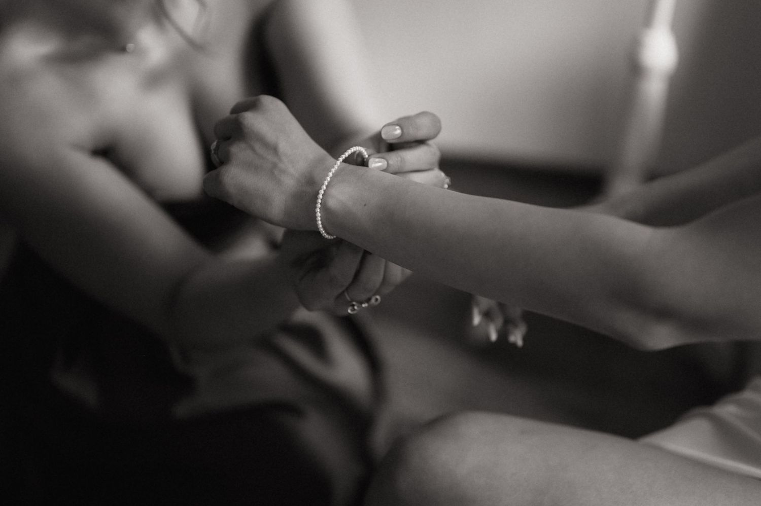 Black and white photo of two people holding hands, one wearing a delicate bracelet, symbolizing connection and intimacy.
