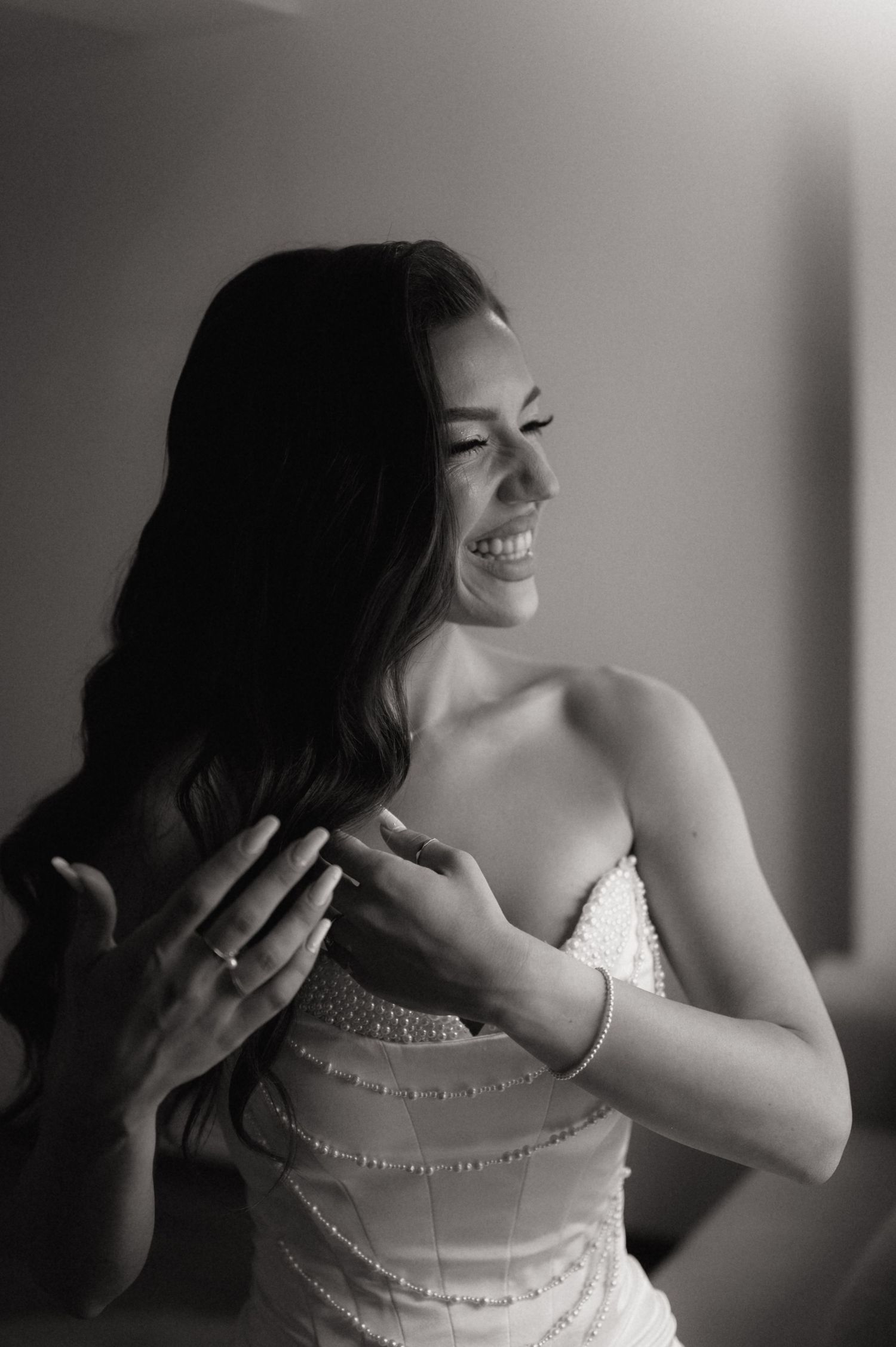 Black and white photo of a smiling bride in a beaded gown, laughing joyfully while getting ready on her wedding day.