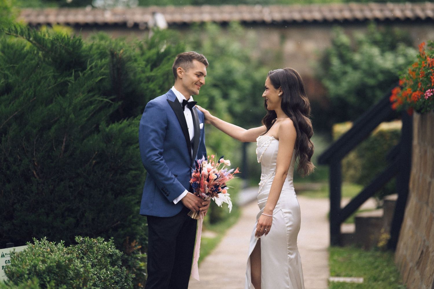 Bride and groom share a tender moment outdoors, with the bride touching the groom's lapel on their wedding day.
