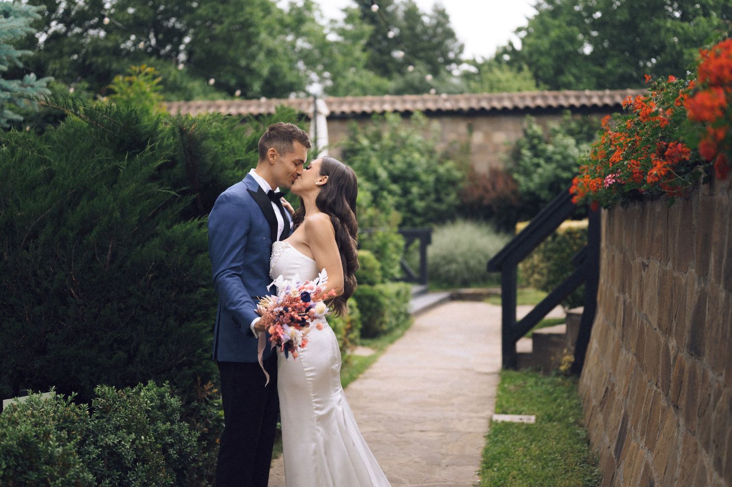 Bride and groom share a romantic kiss in a lush garden setting on their wedding day.