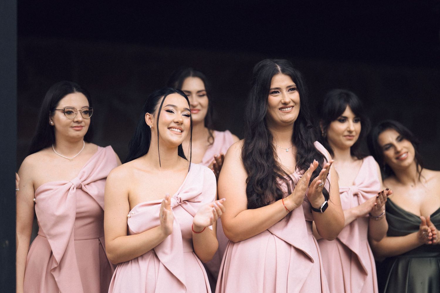 Bridesmaids in pink dresses smiling and clapping at a wedding ceremony.
