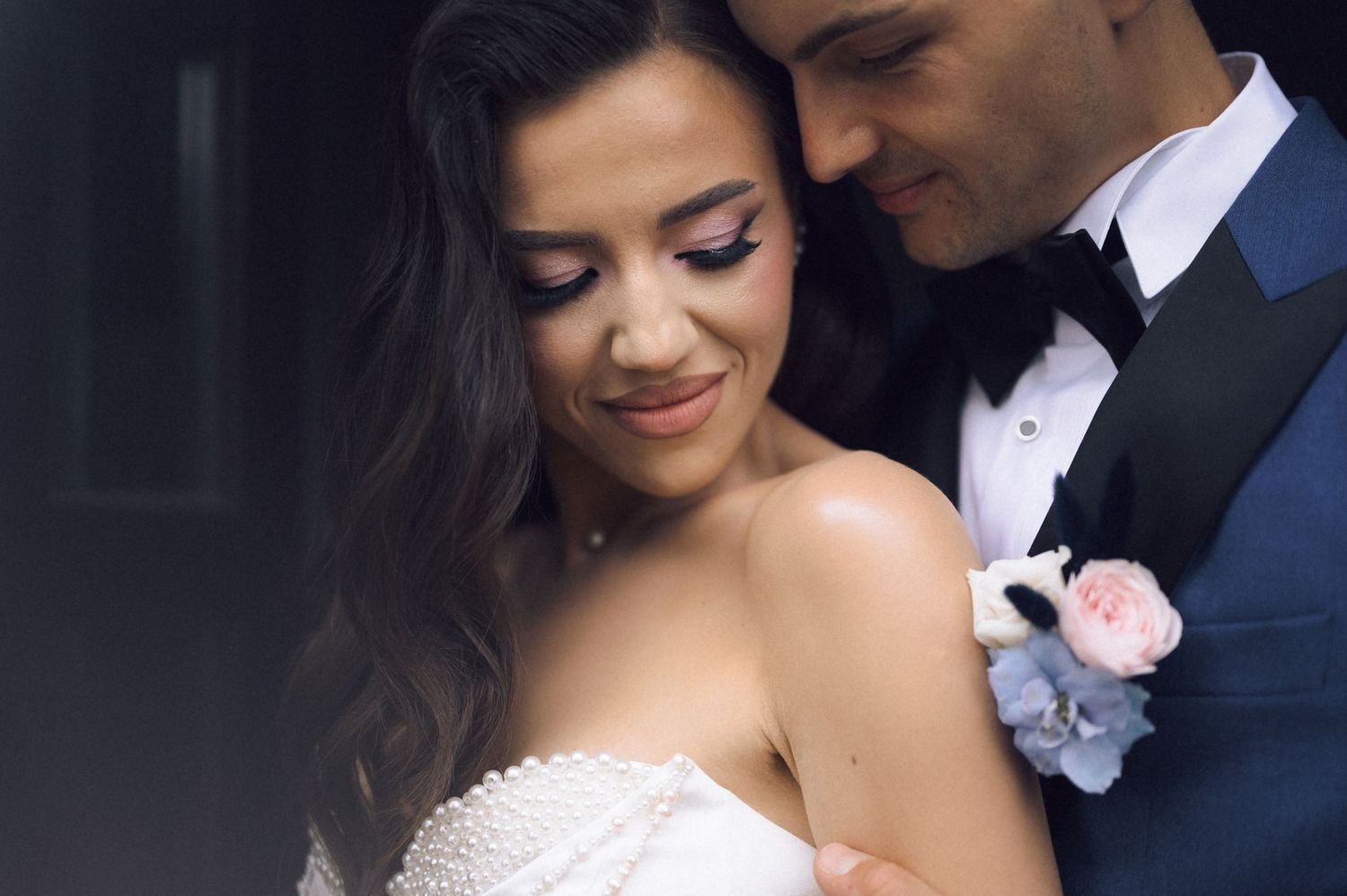 Bride and groom share an intimate moment, with the groom in a navy tuxedo and boutonniere embracing the smiling bride.
