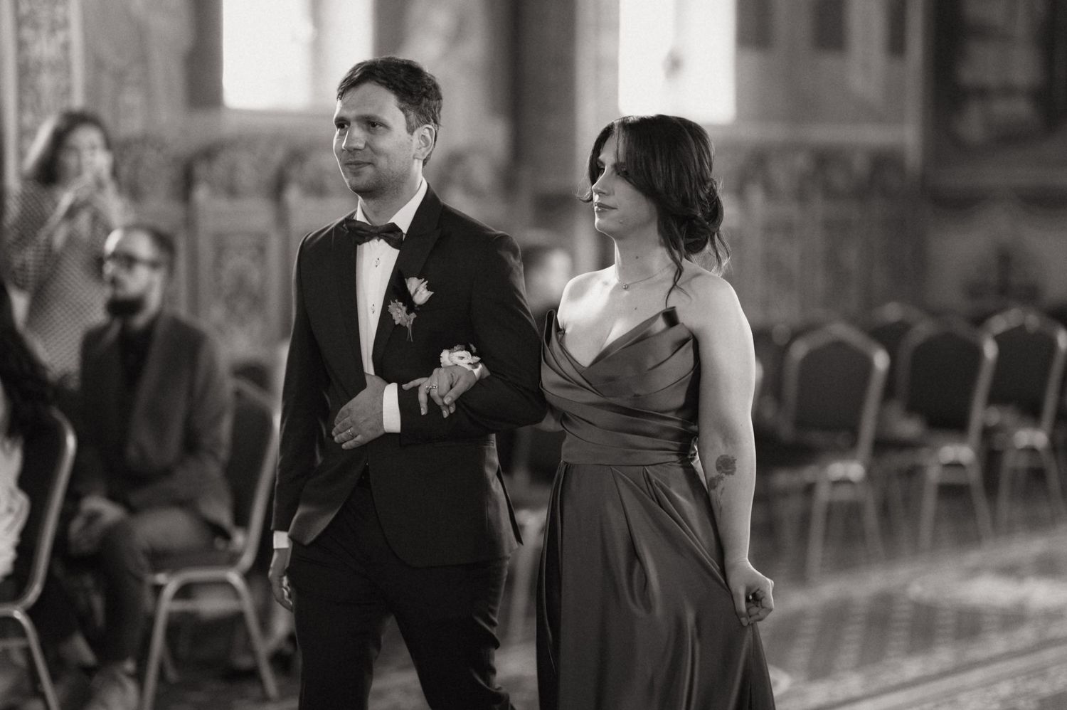 Elegant black and white photo of a couple walking down the aisle at a wedding ceremony in a grand venue.