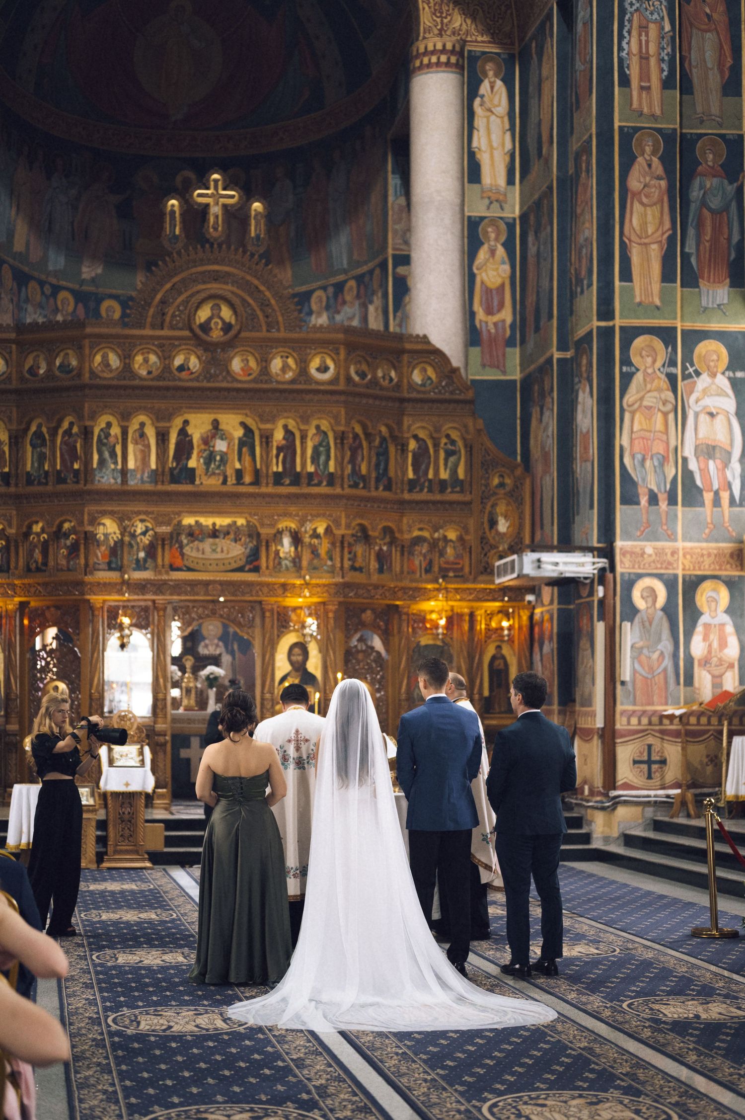 Bride and groom standing at ornate Orthodox church altar during wedding ceremony with gilded iconostasis.