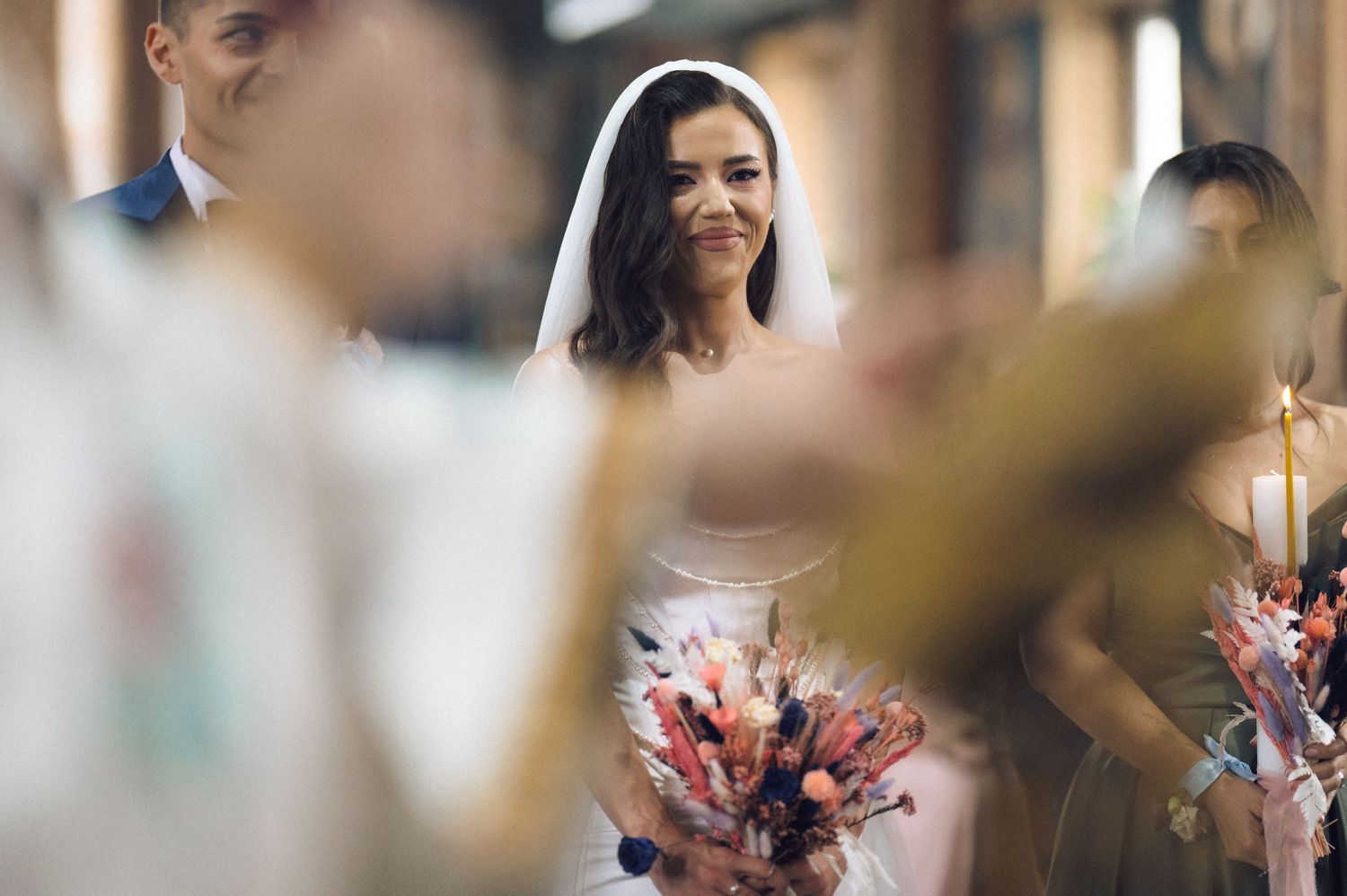 Smiling bride in white gown and veil holds colorful bouquet during a church wedding ceremony.