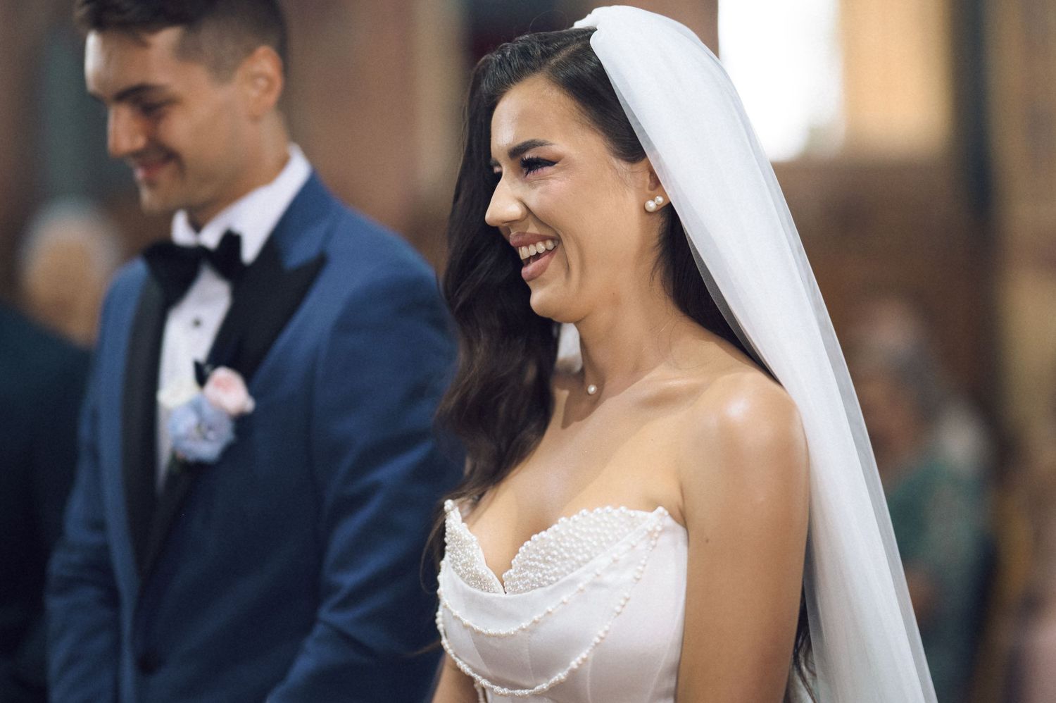 Joyful bride in white strapless gown and veil laughing at church wedding ceremony.