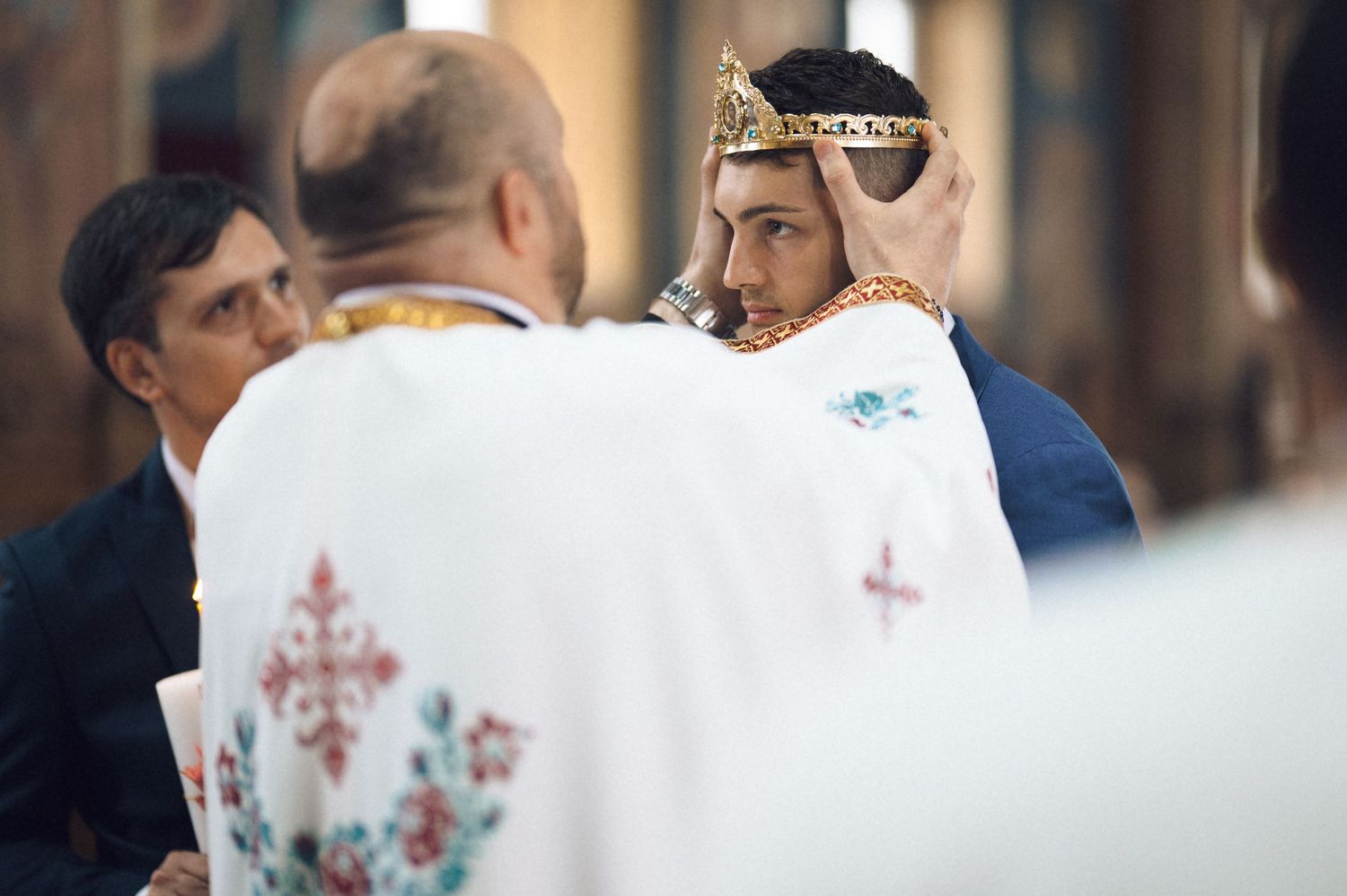 Orthodox priest placing a crown on a young man during a religious ceremony in a church.