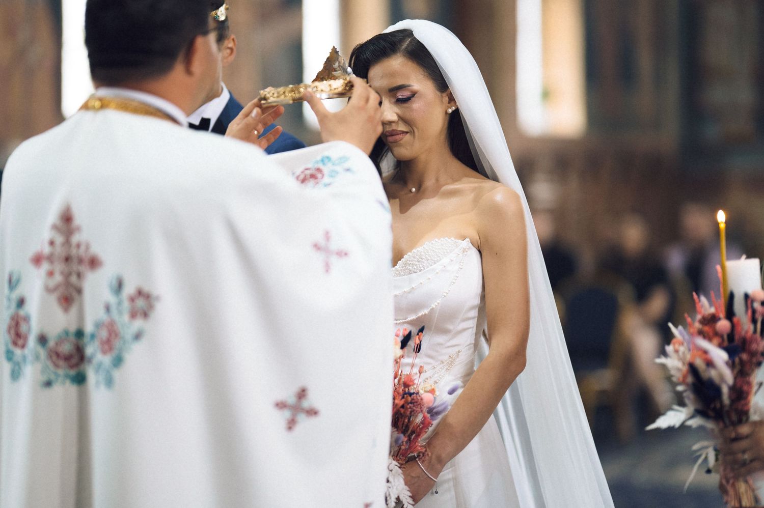 Bride in white gown receives communion from priest during elegant church wedding ceremony.