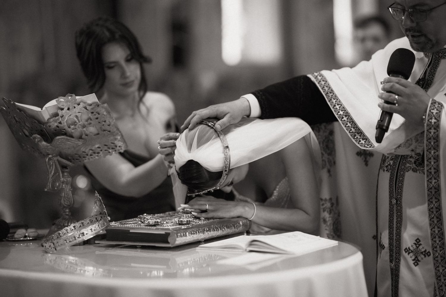 Black and white photo of a Catholic baptism ceremony with a priest pouring water over a bowed head.