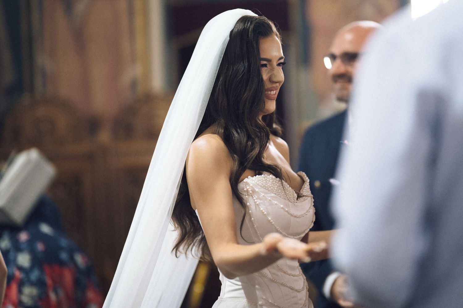 Bride in white wedding dress and veil smiling during church ceremony.