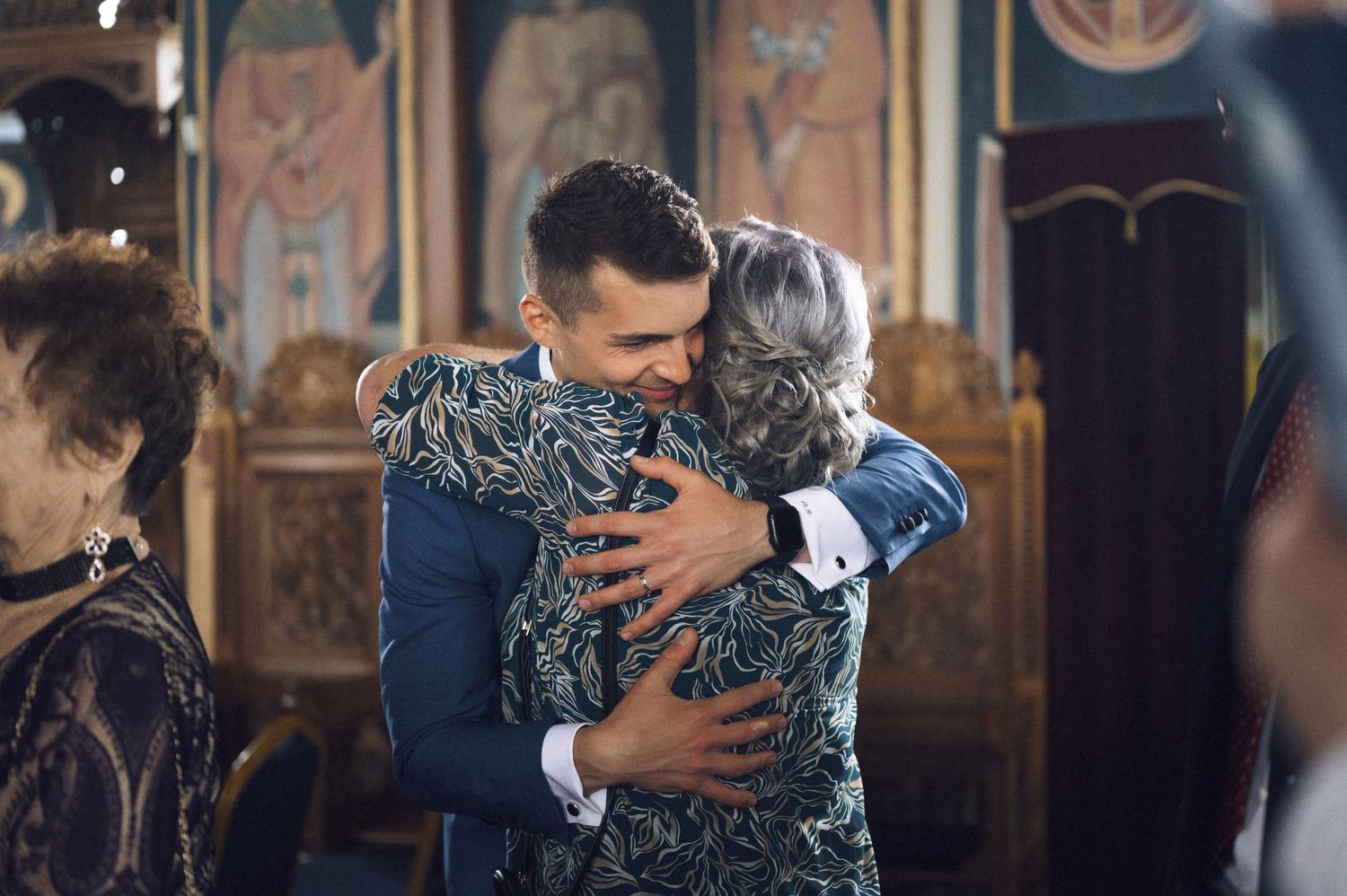 Two people share a warm embrace inside an ornate church during a formal celebration or ceremony.