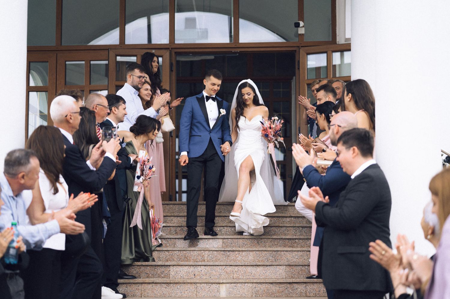 Newlywed couple exits church steps as guests clap and celebrate their wedding ceremony outdoors.