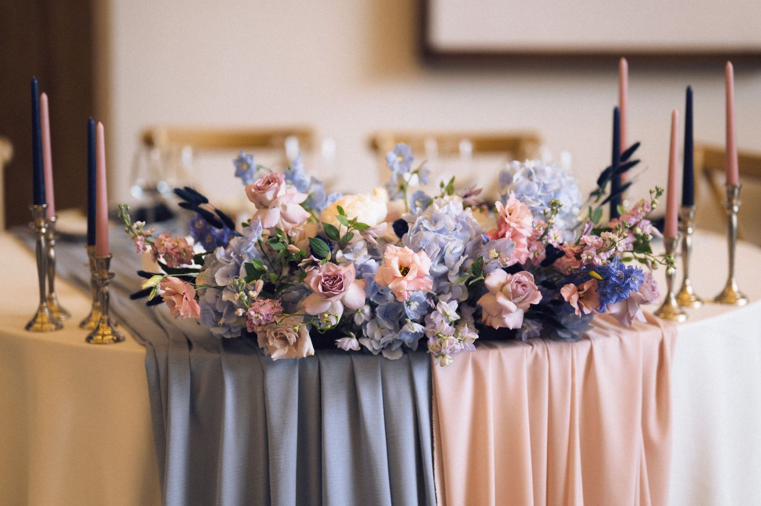 Elegant wedding sweetheart table with blue and pink floral centerpiece and tall taper candles in gold candlesticks.