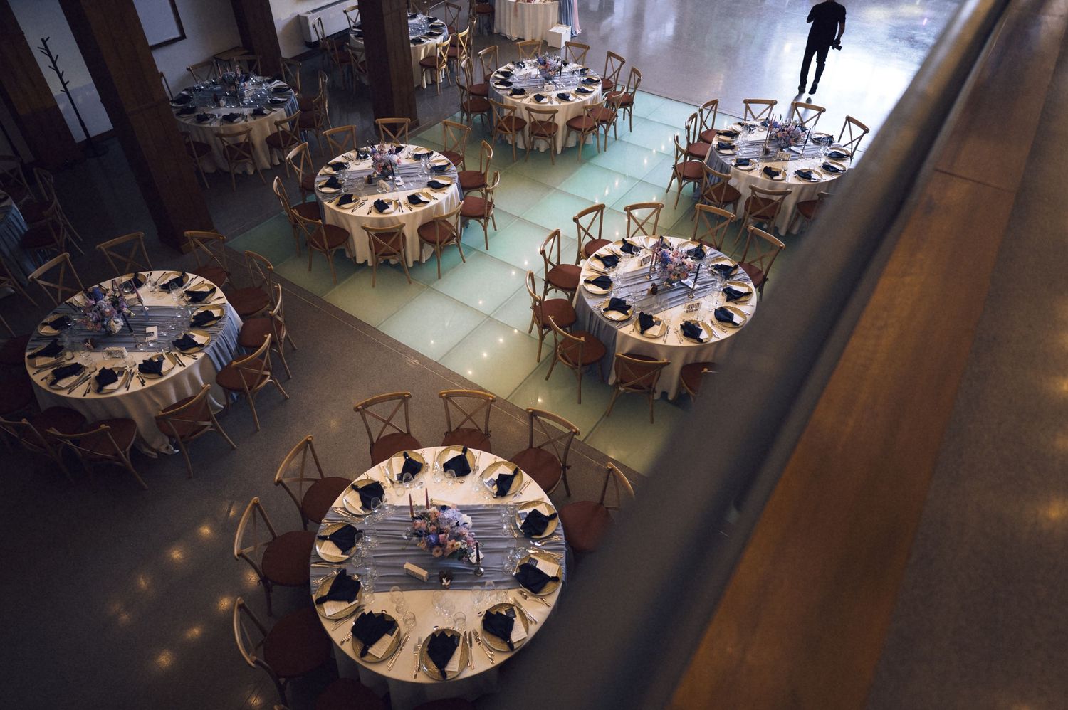 Aerial view of elegant round banquet tables set with white linens and navy napkins in a spacious event hall.