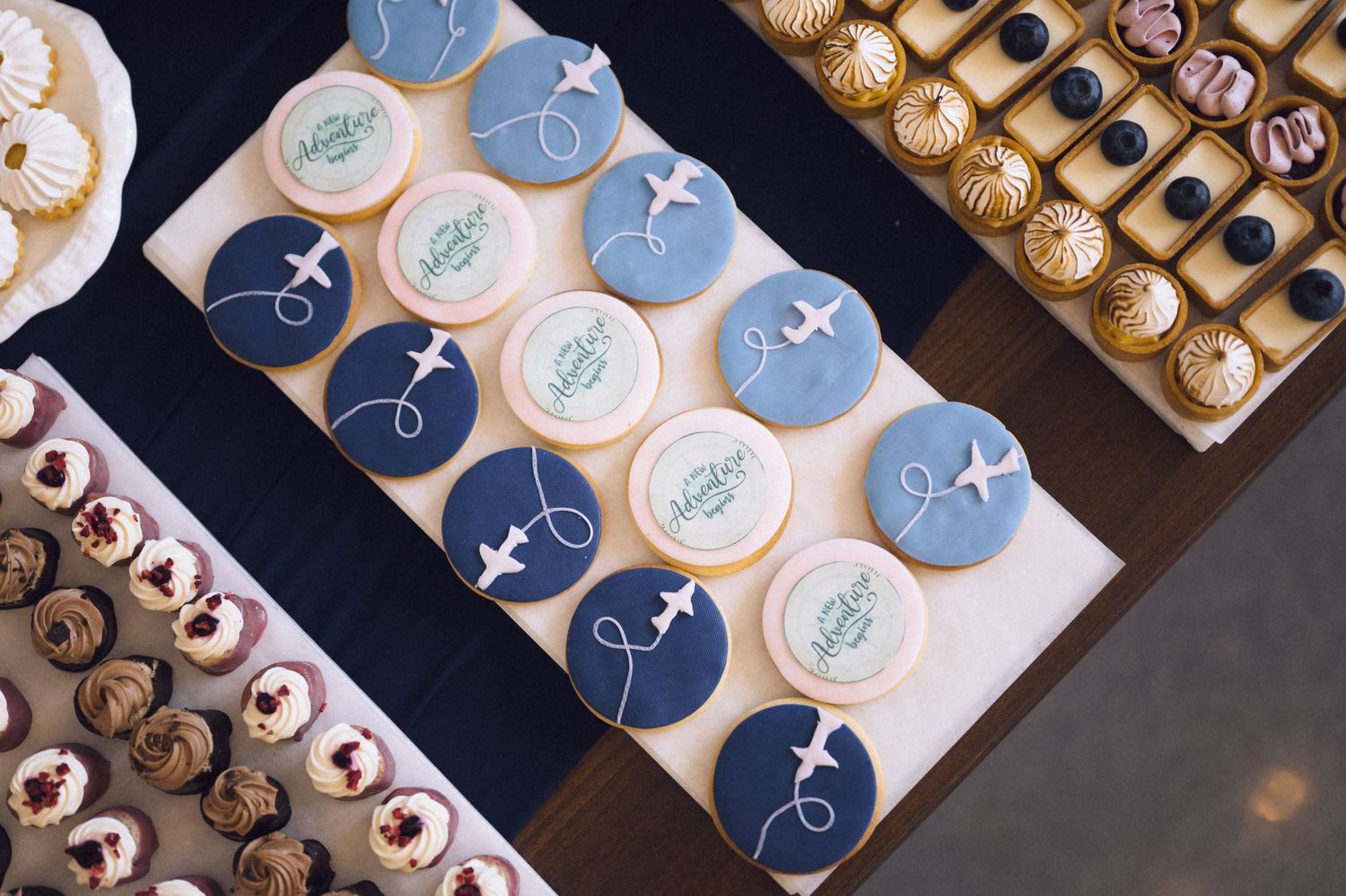 Elegant dessert table with blue and white airplane themed fondant cookies and assorted pastries at an event.