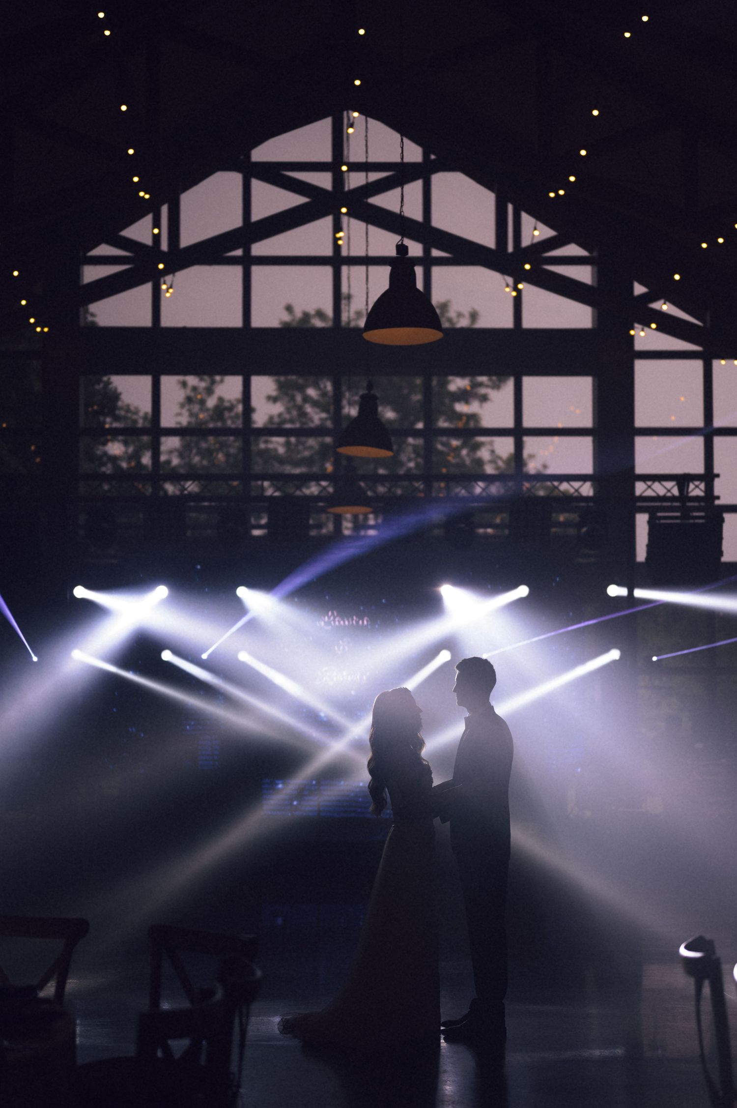 Romantic couple silhouetted against dramatic stage lighting in an elegant venue during their first wedding dance.