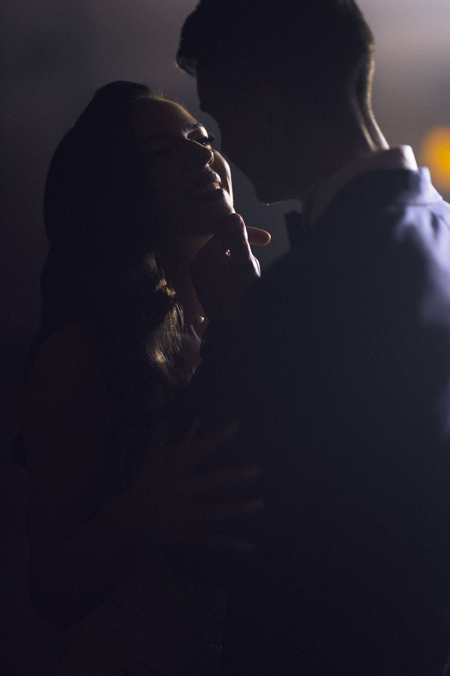 Romantic couple embracing in dramatic dark lighting, silhouetted figures sharing an intimate moment.