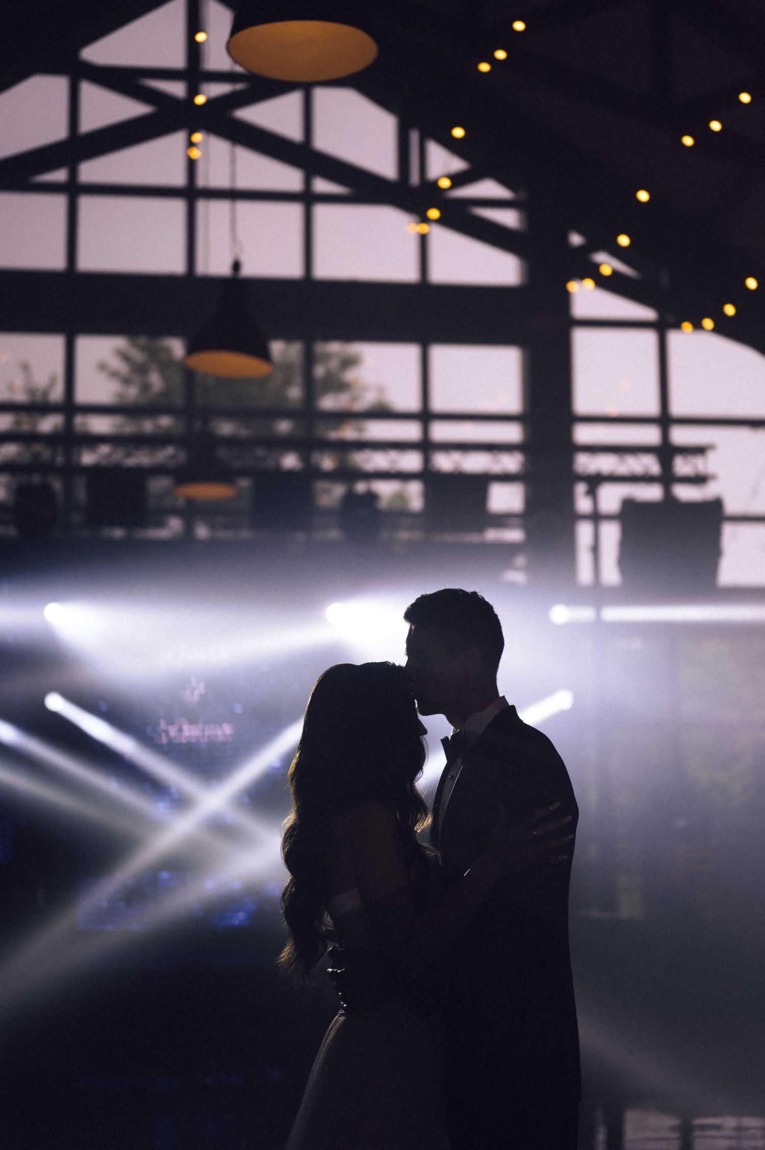 Silhouette of a couple sharing a romantic first dance at a wedding reception with dramatic stage lighting.