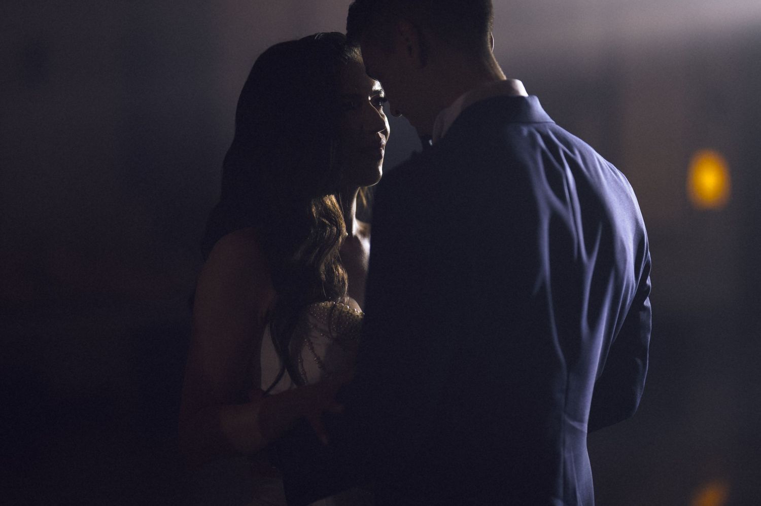 A couple shares an intimate moment in dim lighting, silhouetted against a dark background.