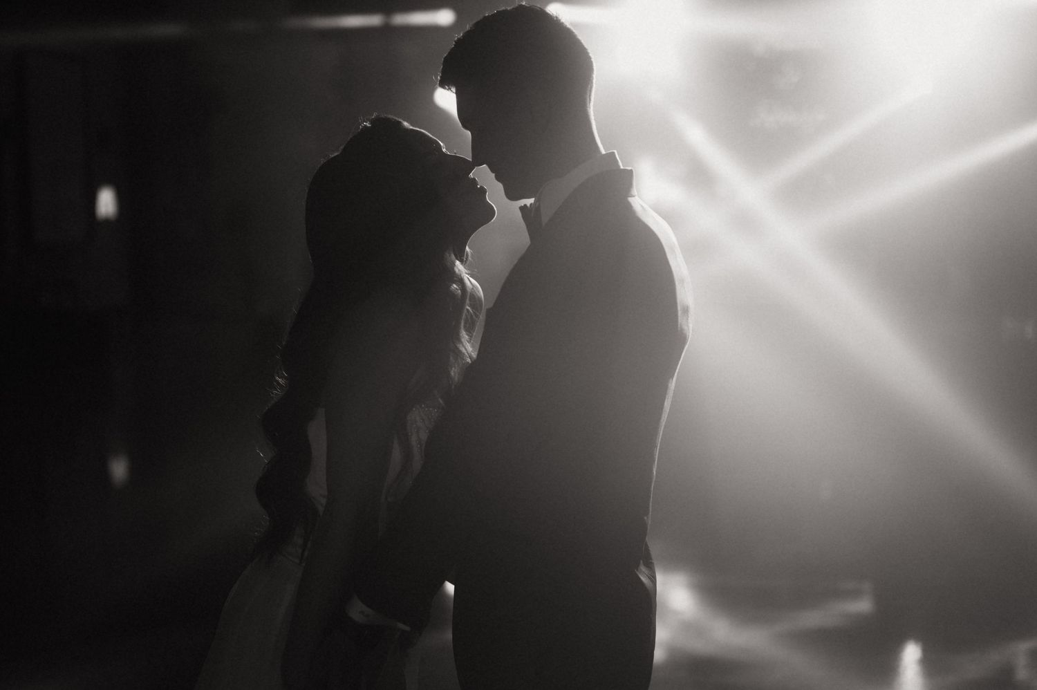 Black and white silhouette of a couple sharing a romantic moment with dramatic backlit rays of light.