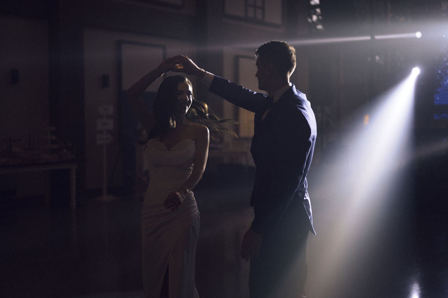 A couple dancing elegantly in a dimly lit room with dramatic spotlight illuminating their romantic dance.