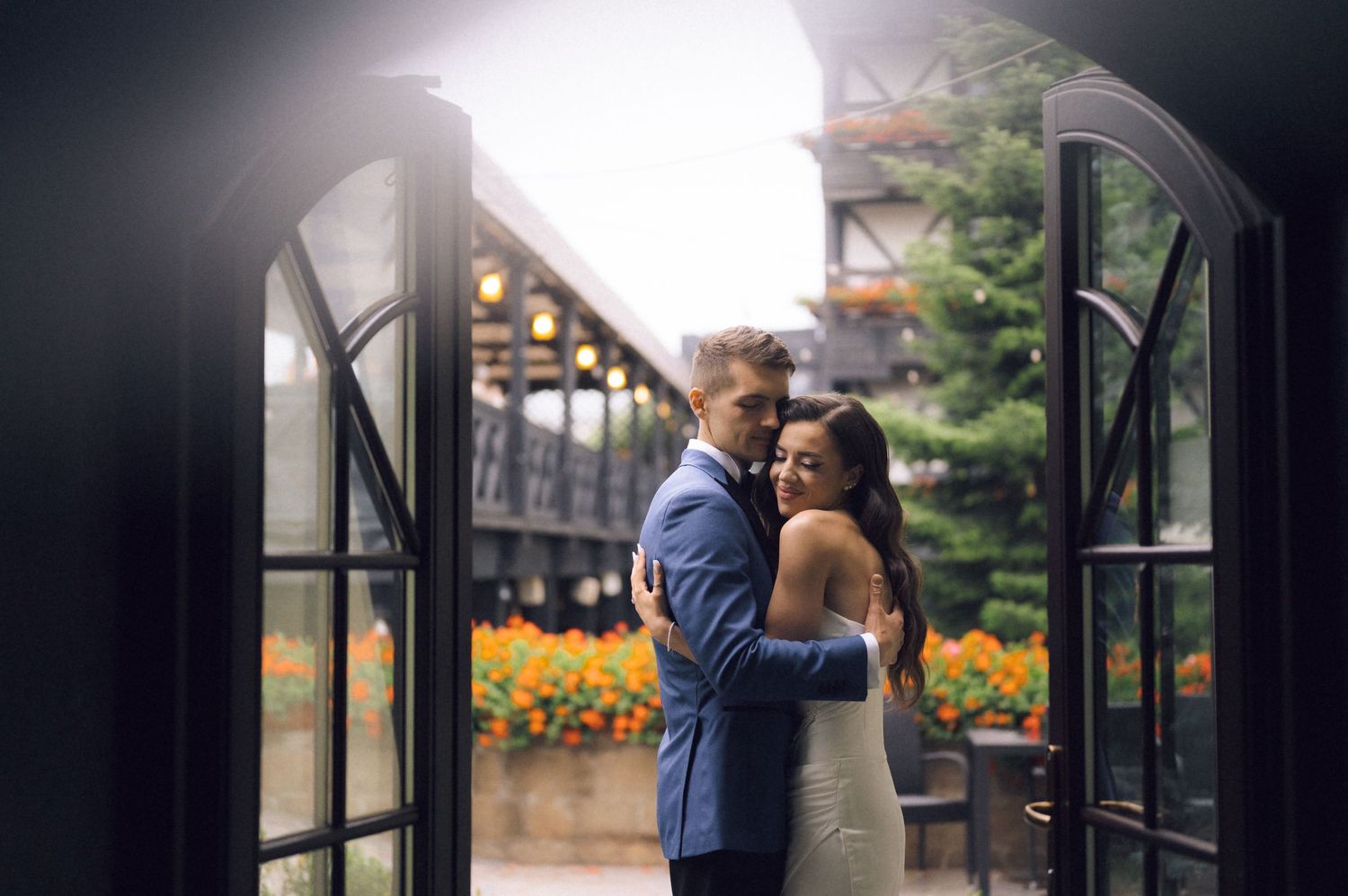 Bride and groom embracing in elegant arched doorway with floral backdrop at romantic outdoor wedding venue.
