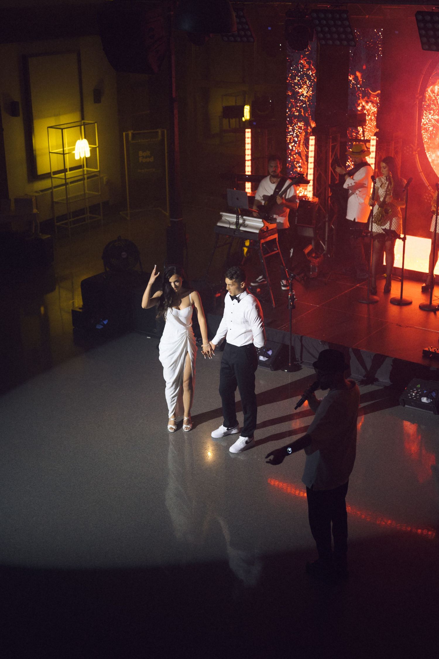 Couple in formal attire dancing on a dimly lit stage with a live band performing in the background.