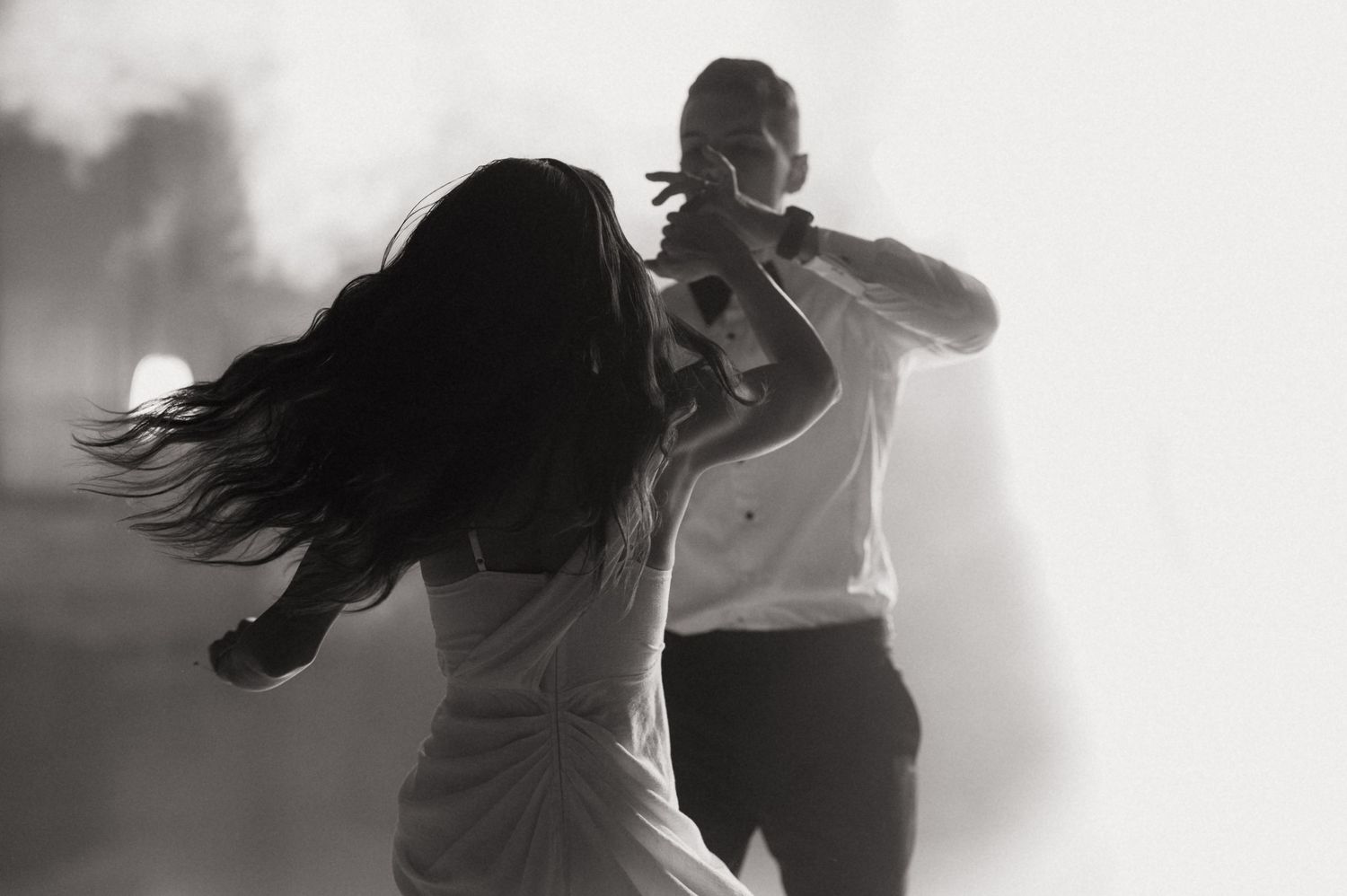 Black and white photo of a couple dancing passionately in misty light, woman's hair flowing dramatically.