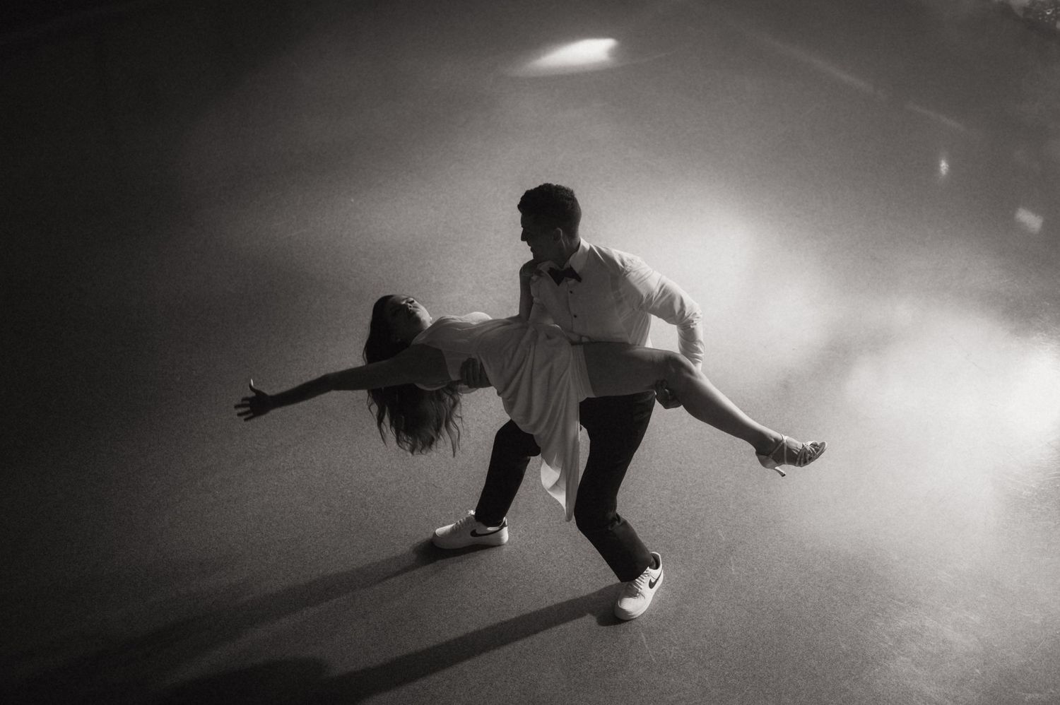Black and white photo of a couple performing an elegant dance move together on a dimly lit stage.