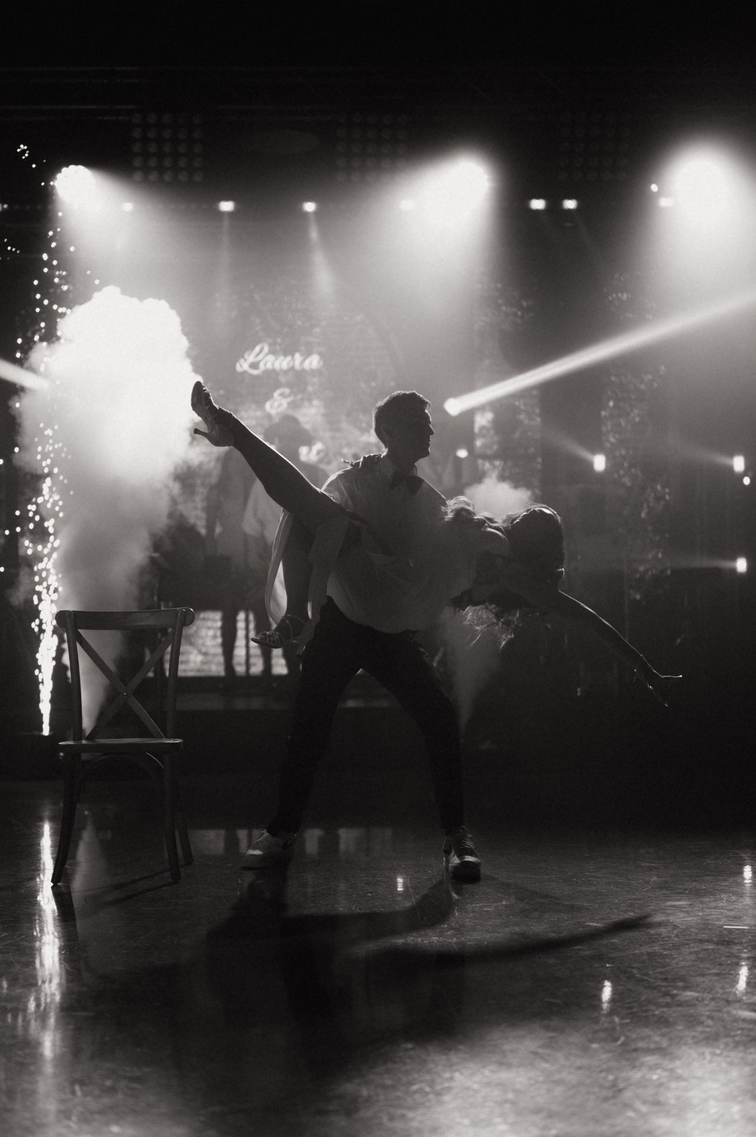 Dramatic black and white photo of dancers performing on a smoky stage with bright spotlights at an elegant event.