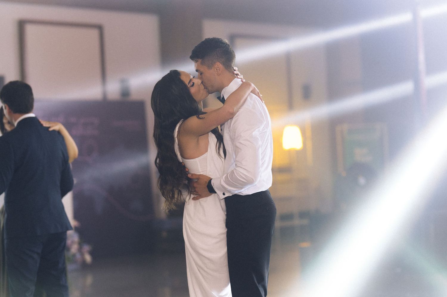 Couple sharing a romantic first dance at their wedding reception under soft spotlight beams.