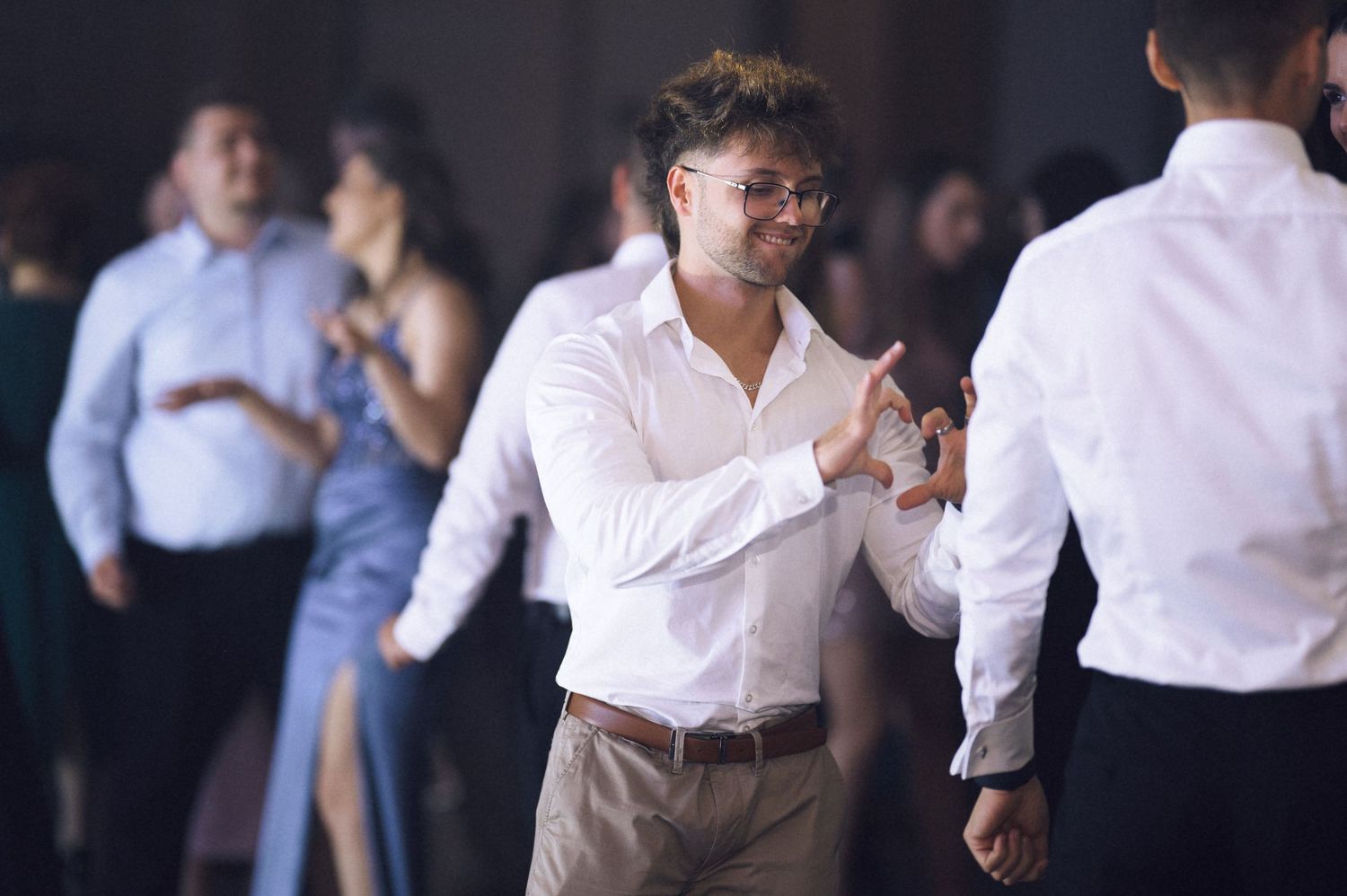 Two men dancing together at a formal event, with guests socializing in the background.