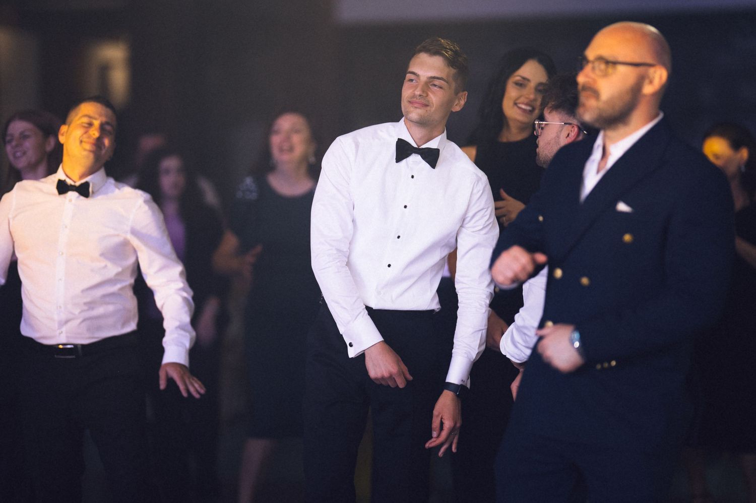 Men in tuxedos dancing at a formal wedding reception party on the dance floor.