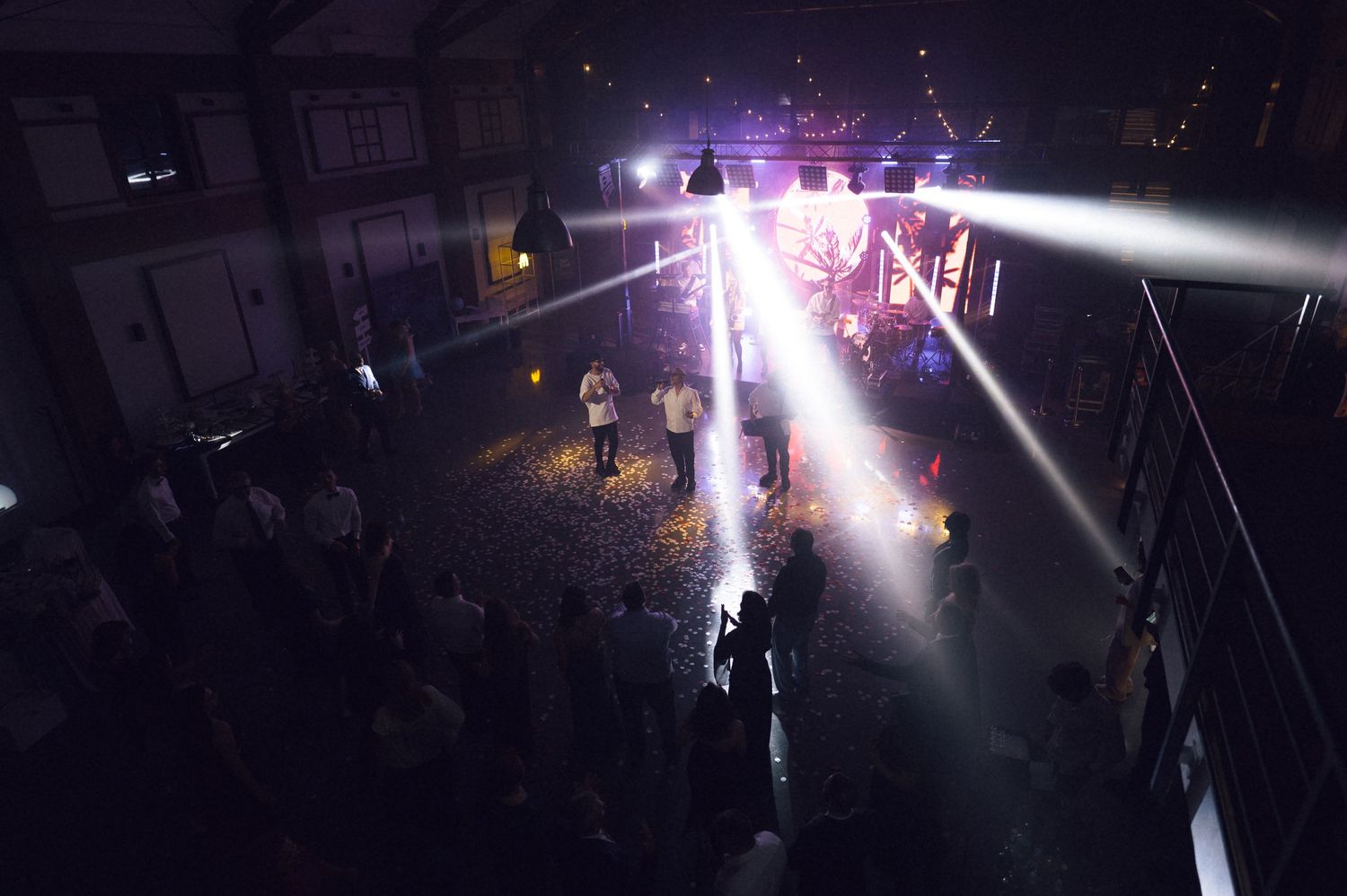 Aerial view of a dark concert venue with dramatic stage lighting beams over crowd.