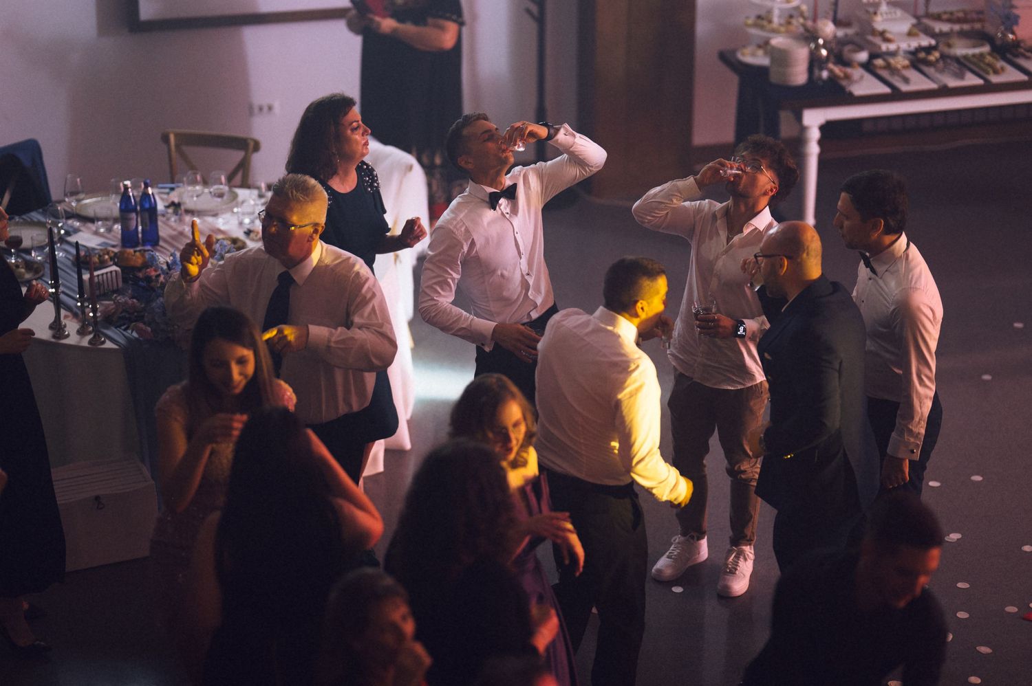 People dancing and socializing at an indoor party event with warm lighting and a bar in the background.
