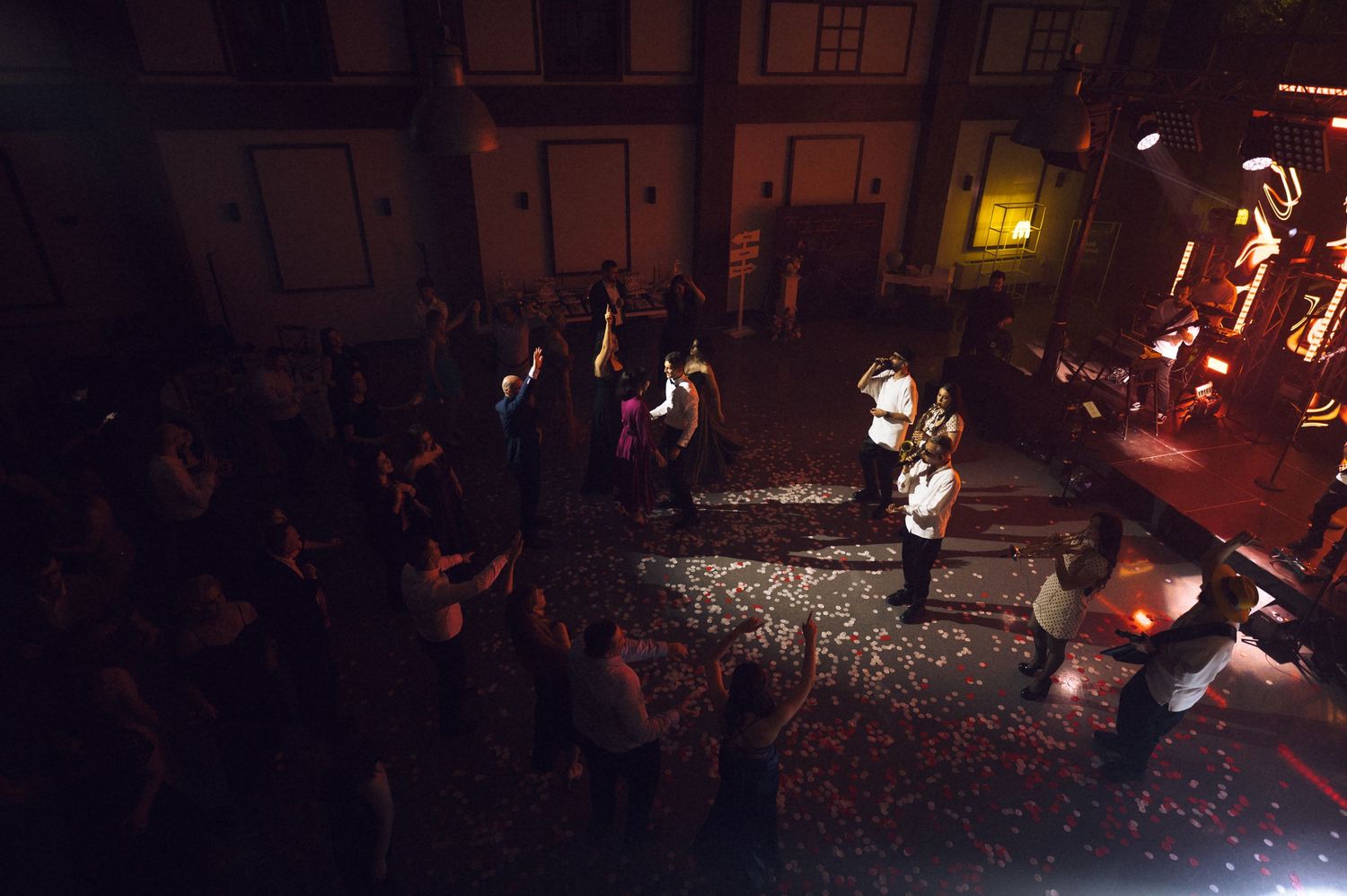 Aerial view of a lively nighttime outdoor event with crowd and performers illuminated by warm lights.