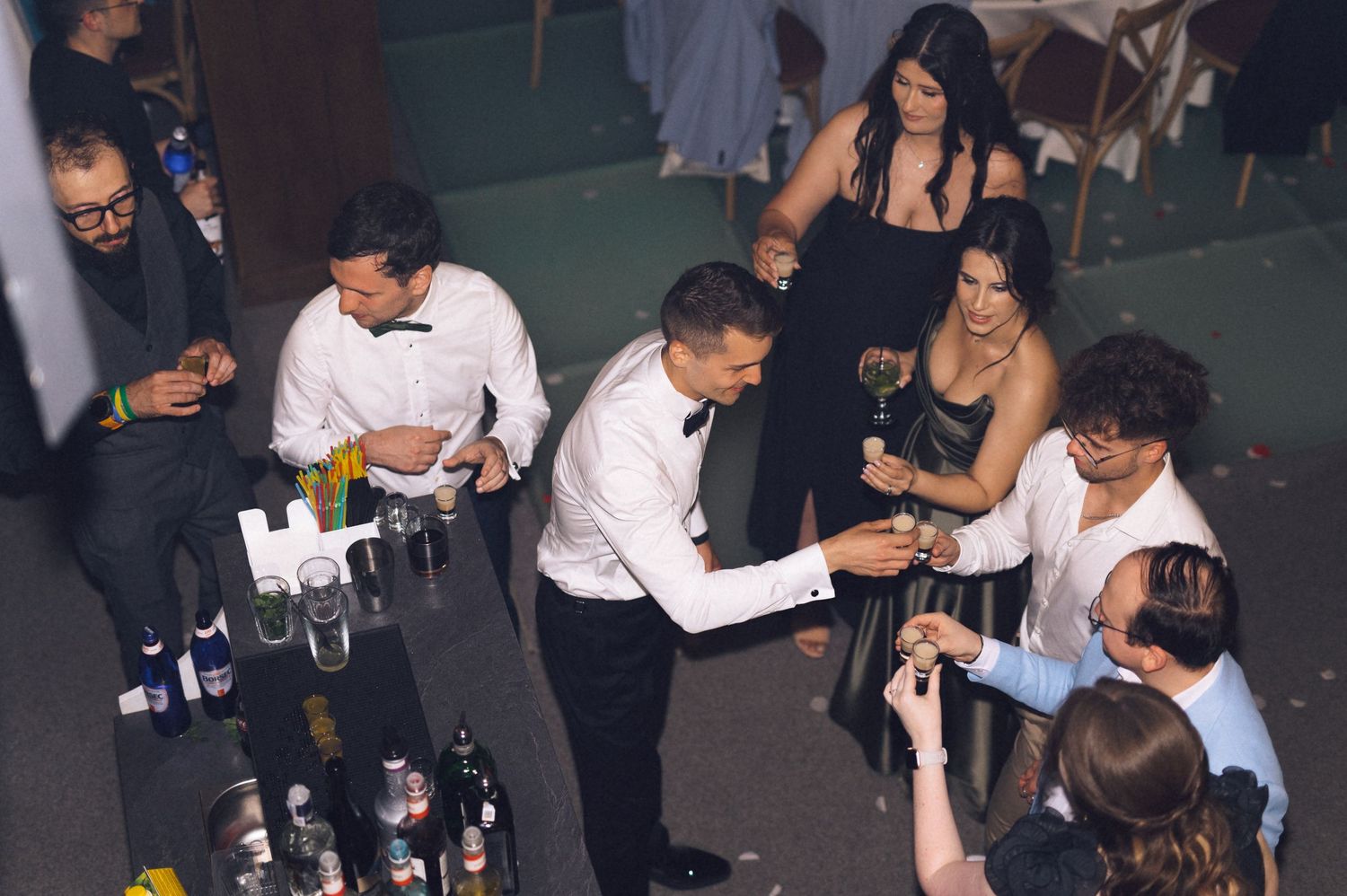 Guests mingle at an elegant event bar, with a bartender in a tuxedo serving drinks to attendees in formal attire.