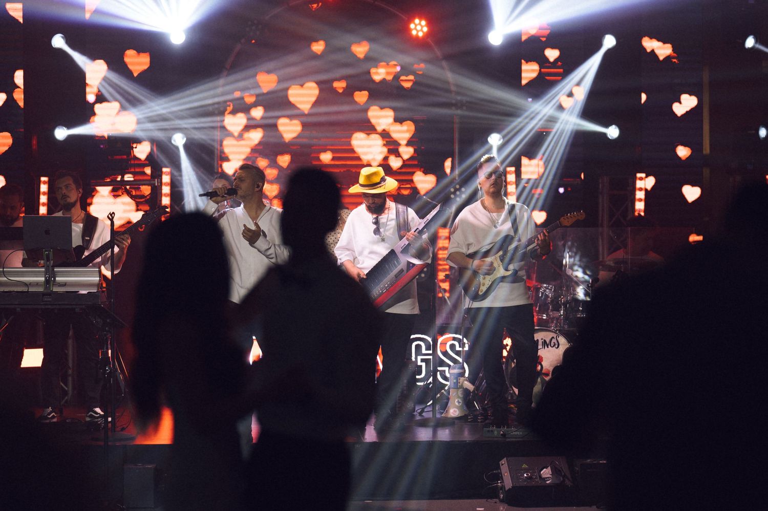 Live band performing on a decorated stage with heart-shaped lights and dramatic beams at an evening event.