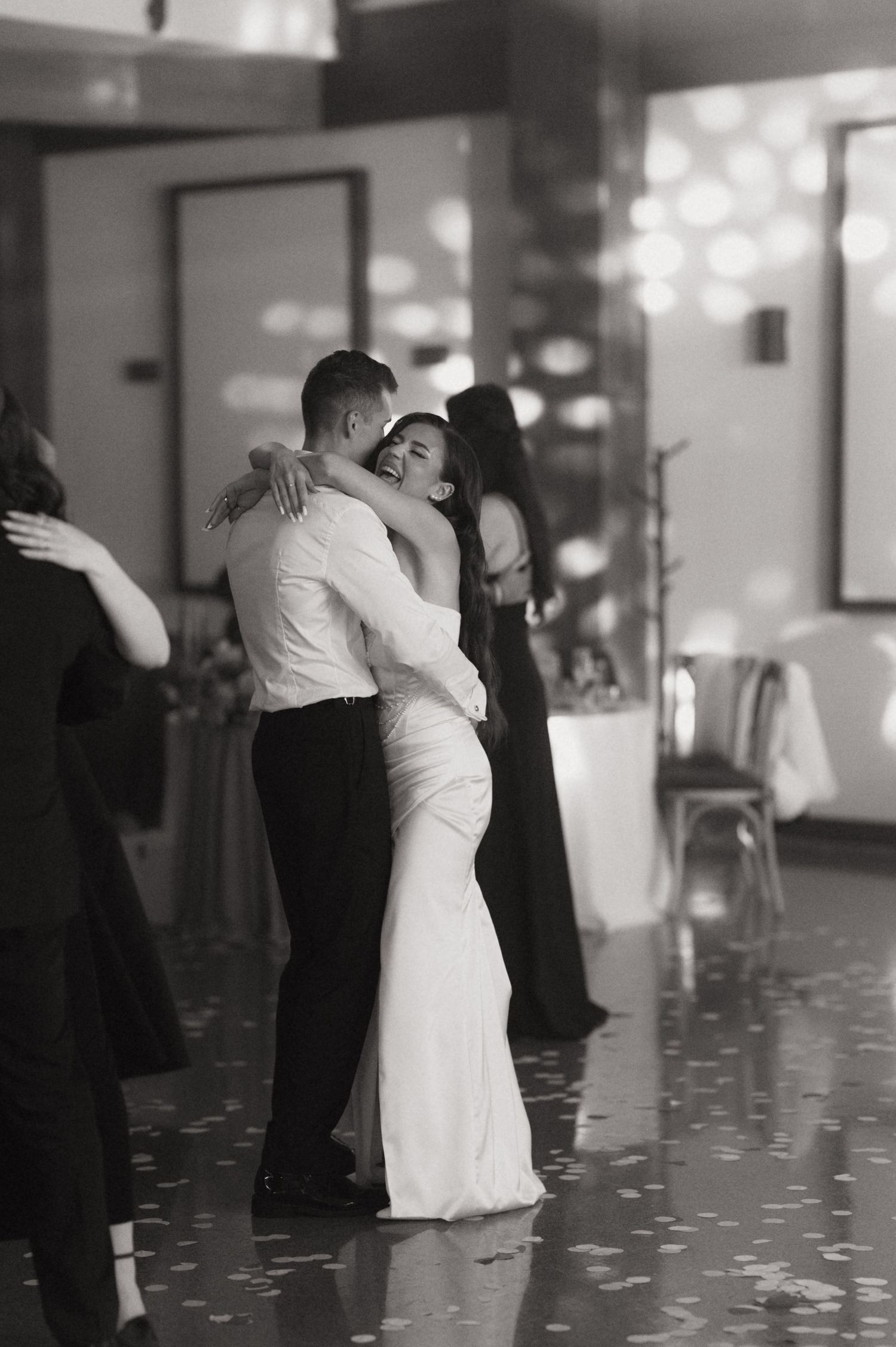 Black and white photo of a couple sharing their first dance at a wedding reception, bride in white gown smiling joyfully.