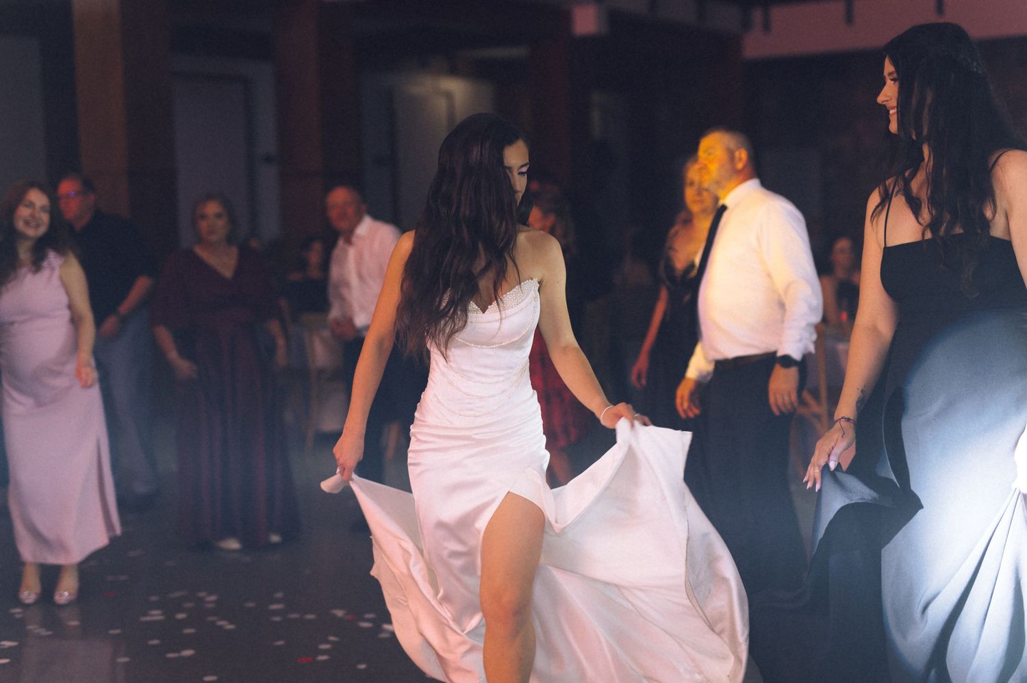 Bride in white gown twirling on wedding reception dance floor surrounded by guests in elegant attire.