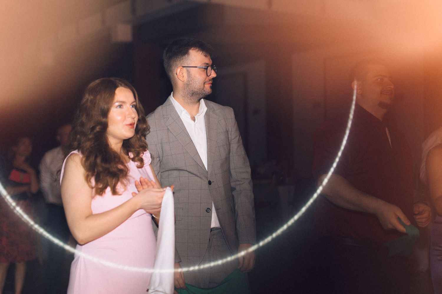 A woman in pink and a man in a gray suit stand together at an event, illuminated by a circular LED light display.