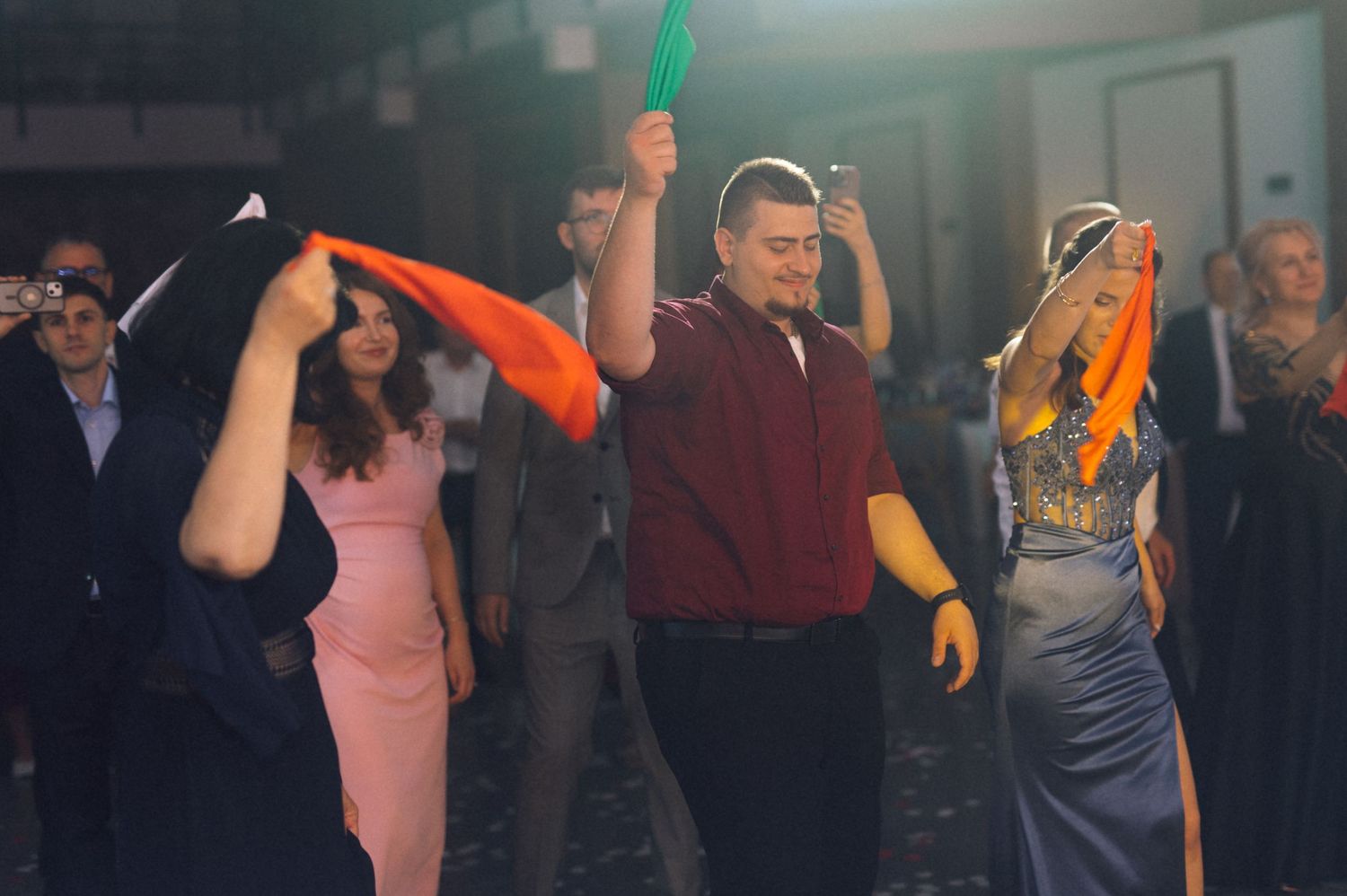 People dancing at a party, waving colorful scarves under bright lights in a festive indoor celebration.